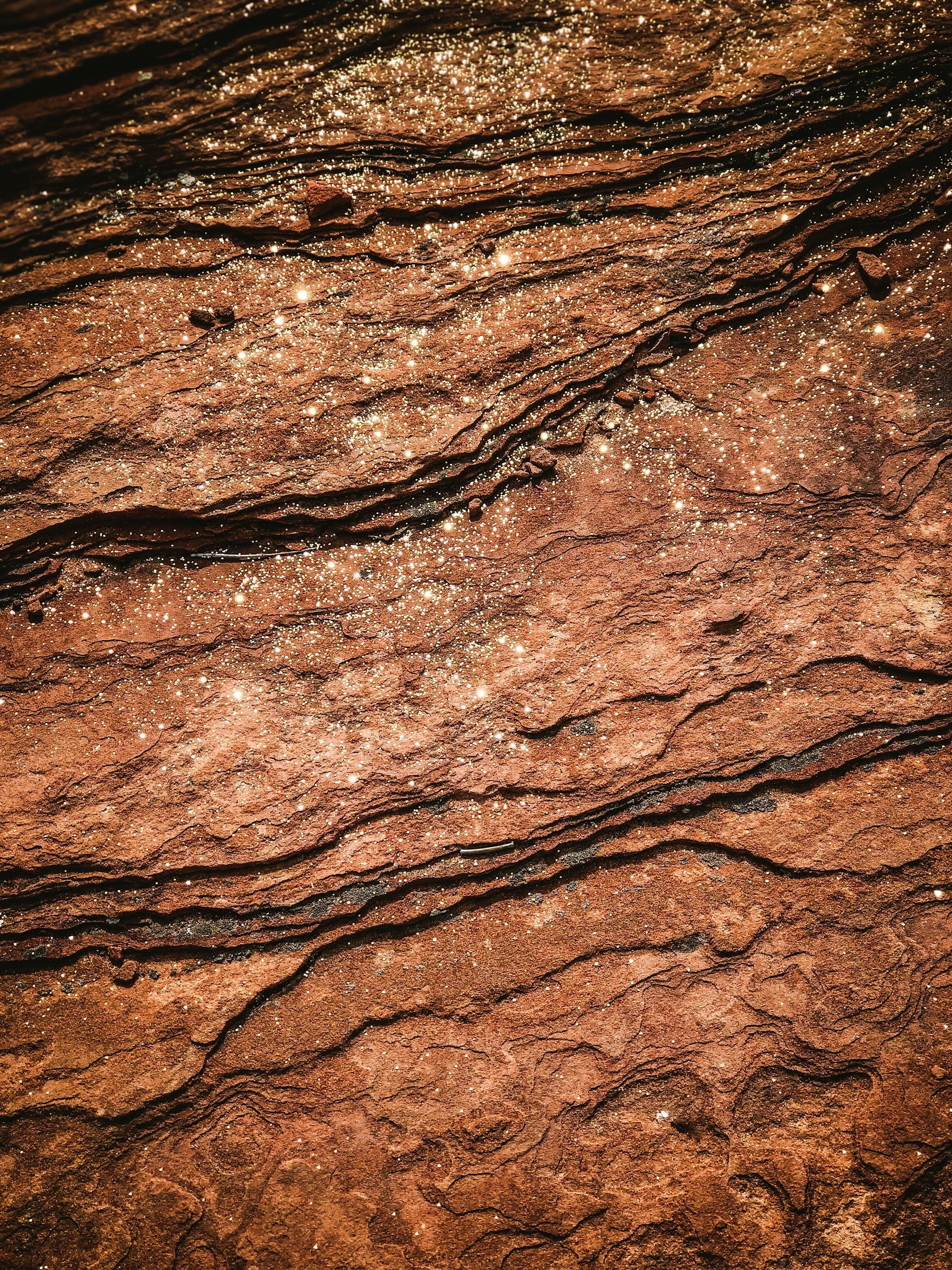 Close-up of rusted, layered rock surface with shiny crystals or mineral deposits.