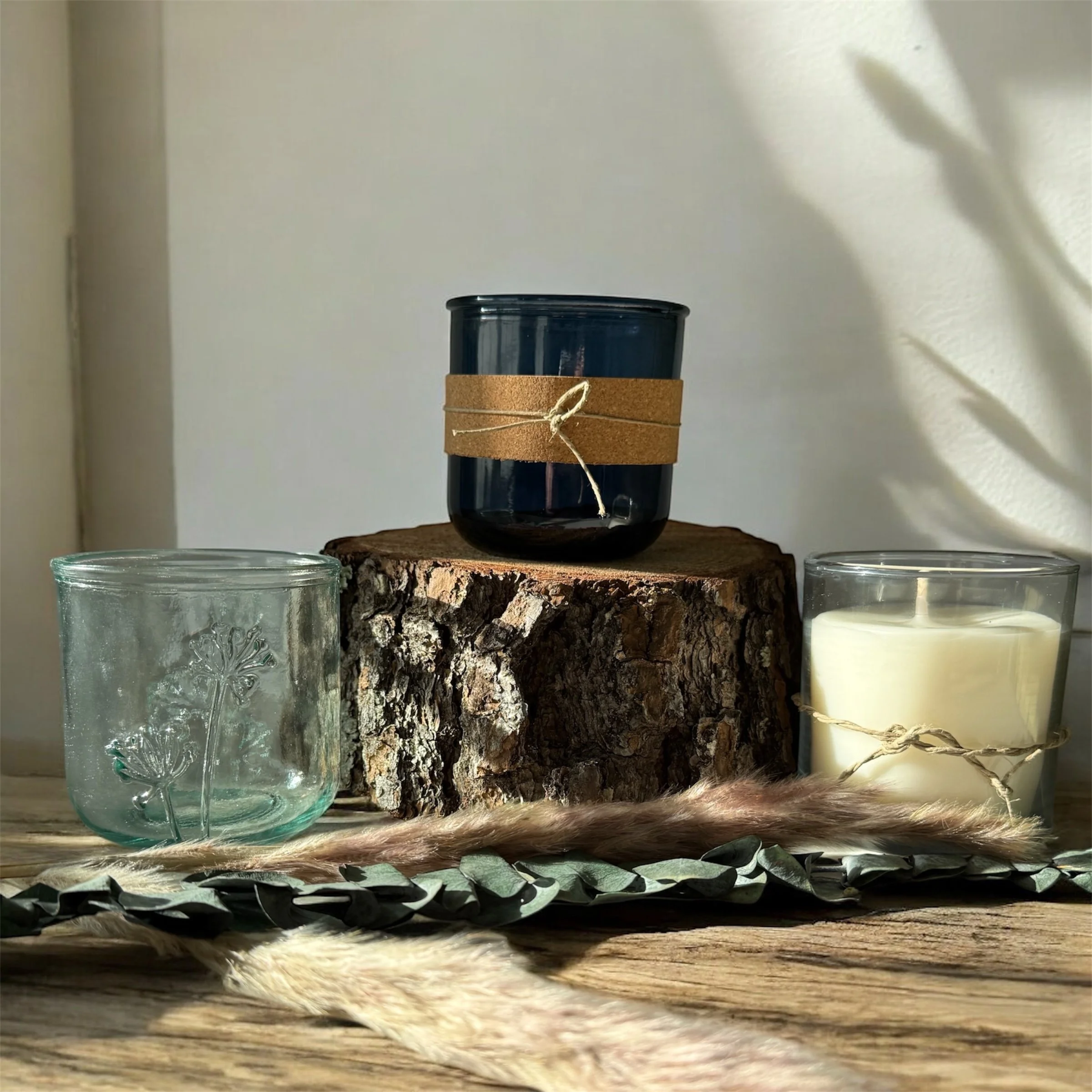 Decorative candles and recycled glass vessels arranged on a wooden surface with natural light.
