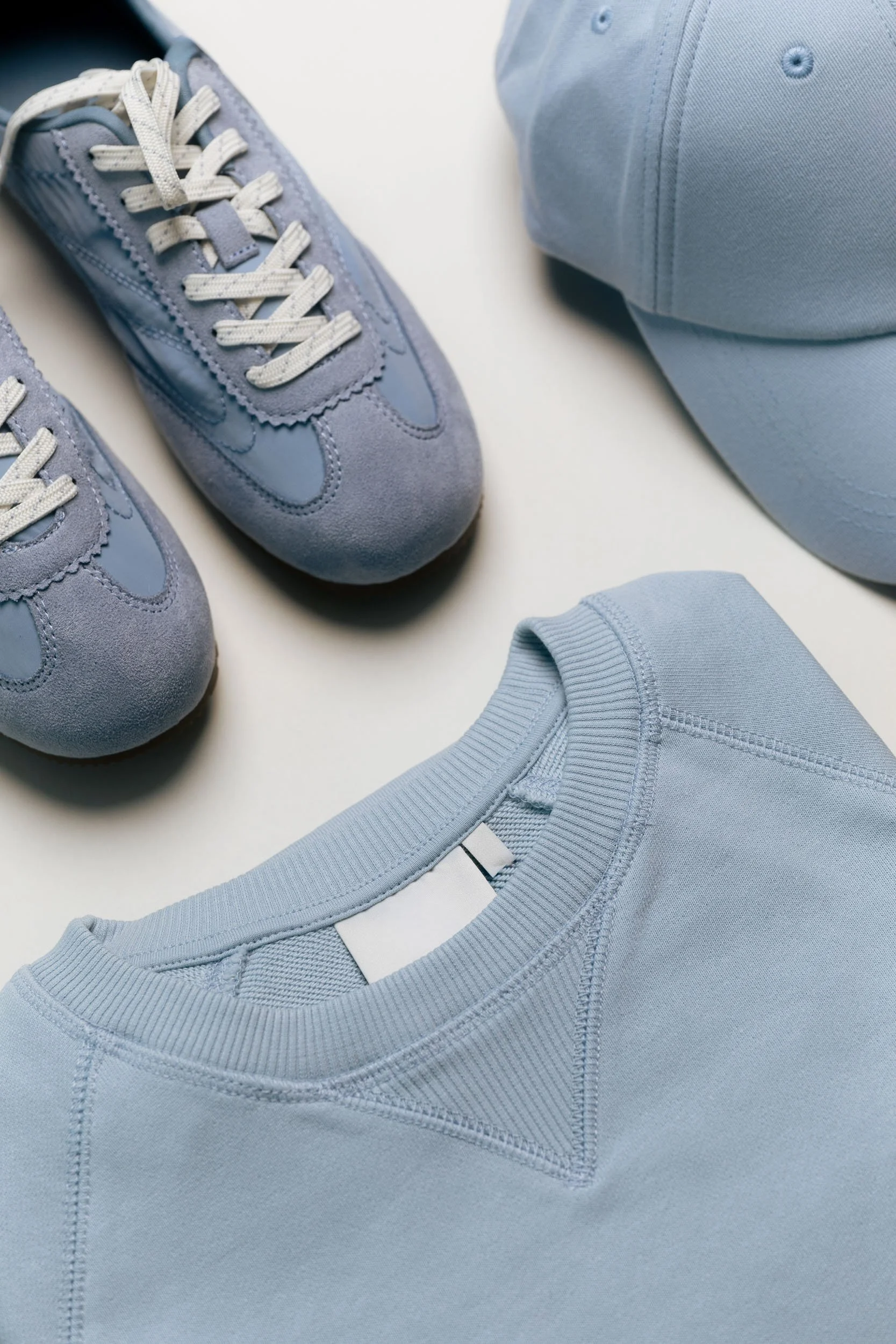 Light blue athletic shoes, sweatshirt, and cap on a white surface.