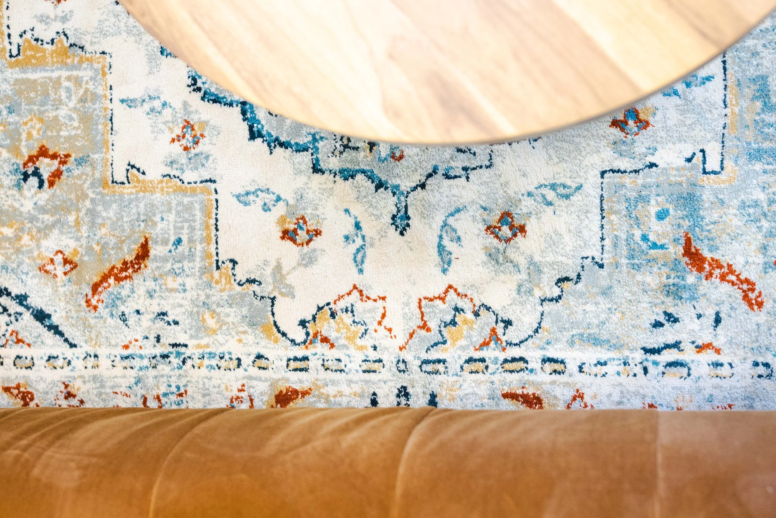 View from above of a patterned area rug under a wooden table and tan-colored chairs.