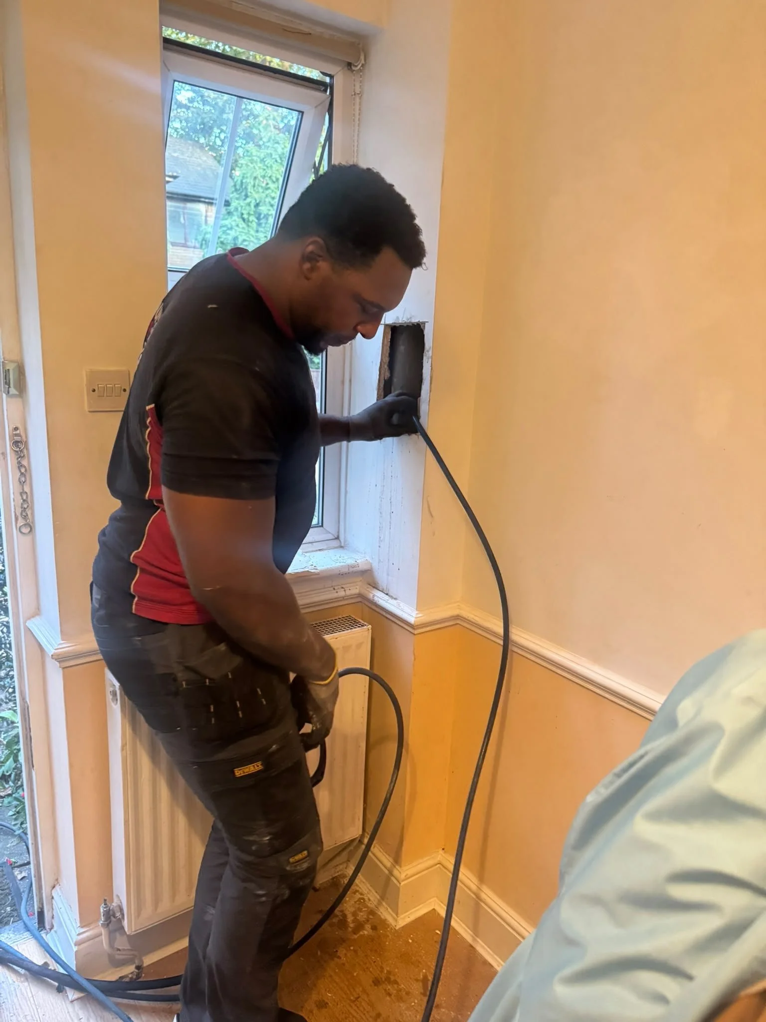 Under Pressure Plumbing engineer using a flexible drain-cleaning cable through an internal wall access opening to clear a blocked drainage pipe.