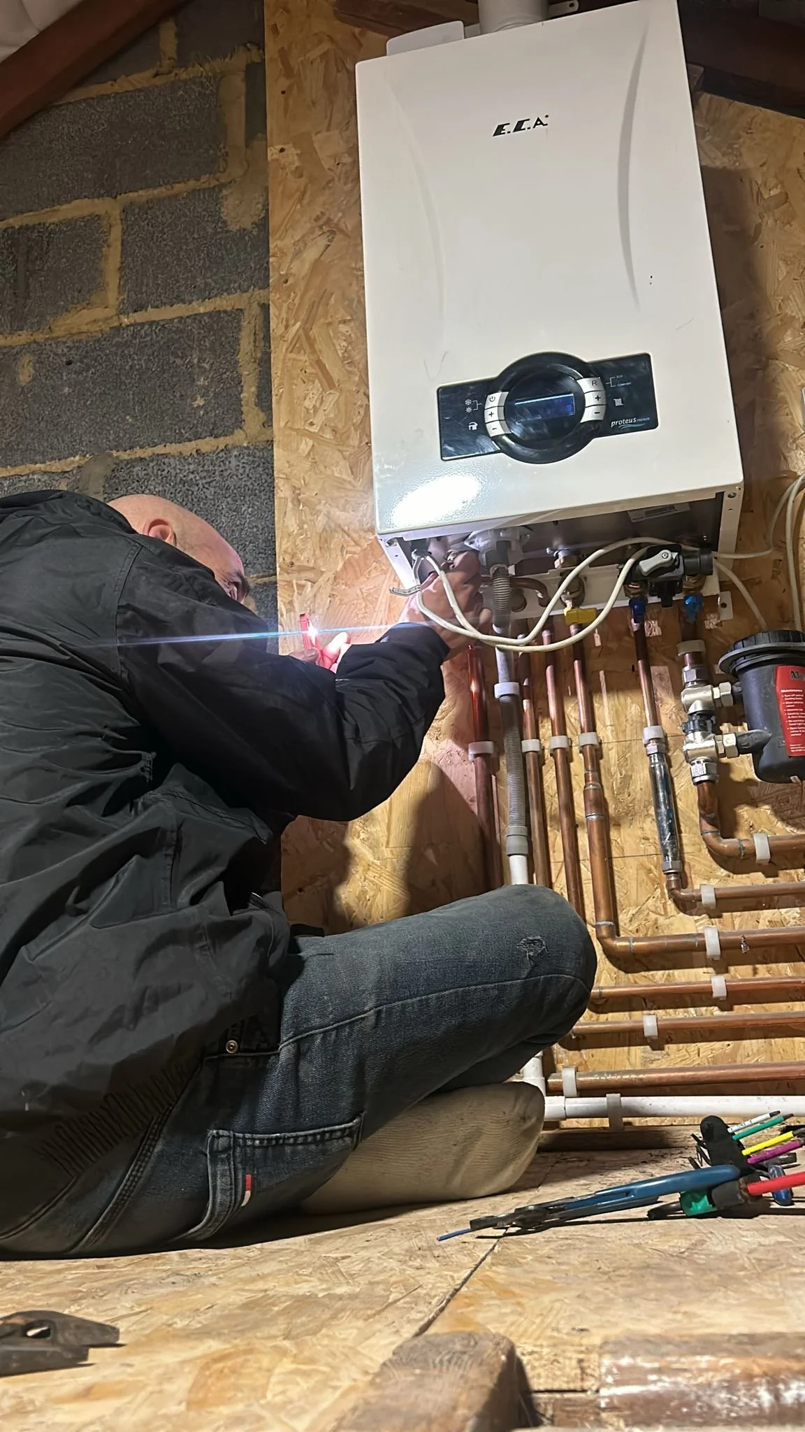 Heating engineer working on pipework beneath a wall-mounted boiler