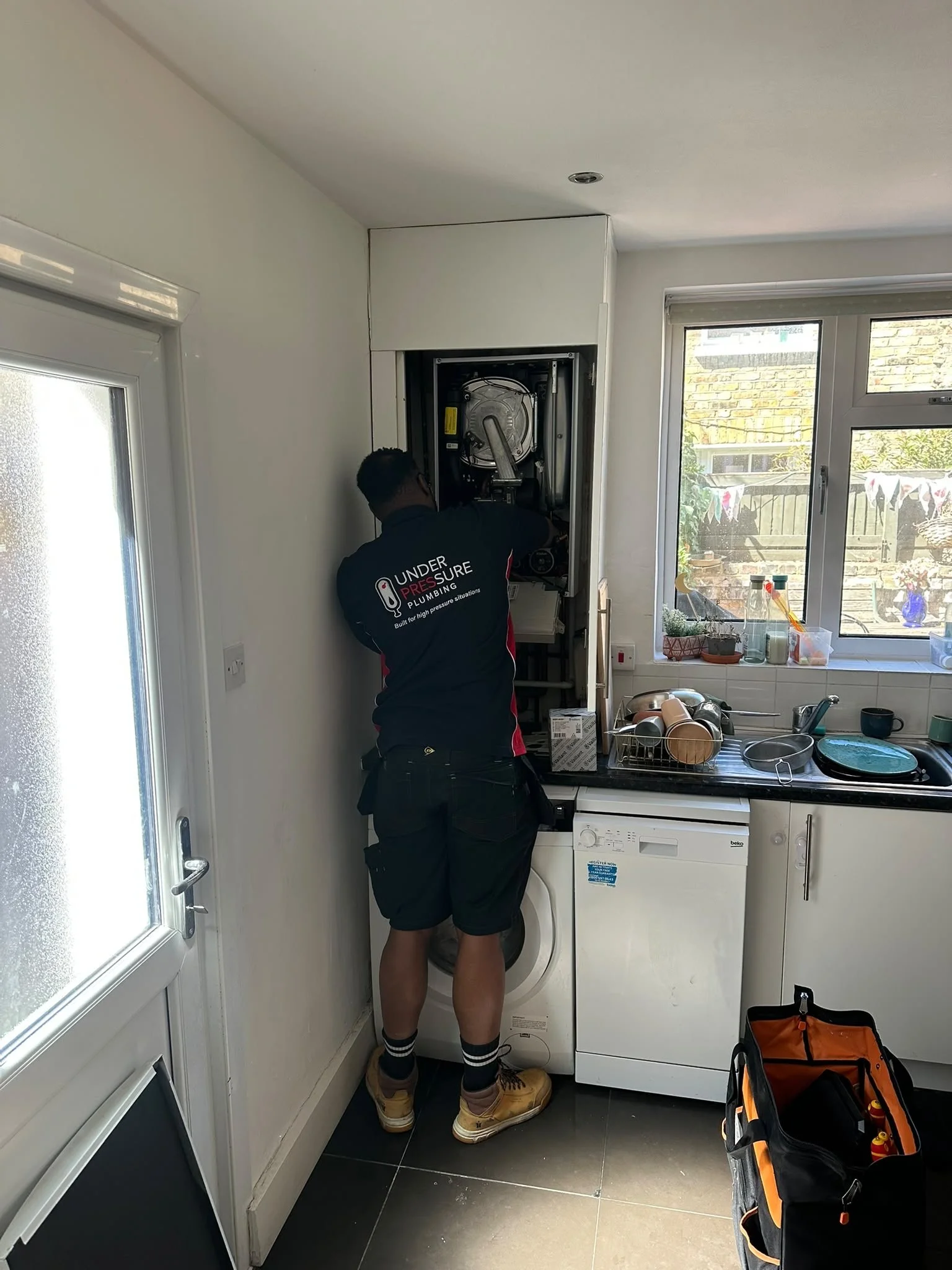 Under Pressure Plumbing heating engineer servicing a wall-mounted gas boiler in a residential kitchen.