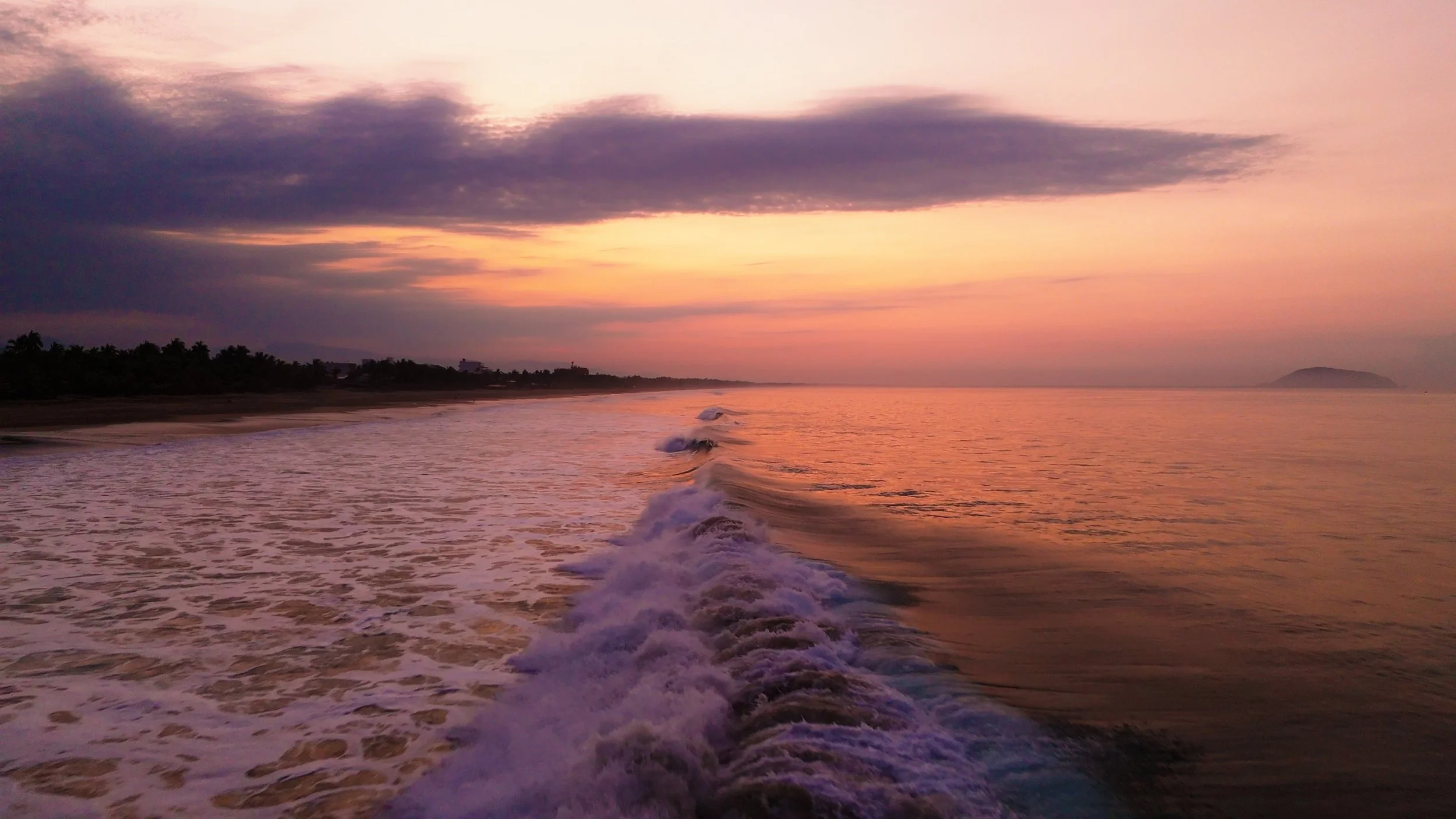 Sunset over the ocean with gentle waves and a distant island