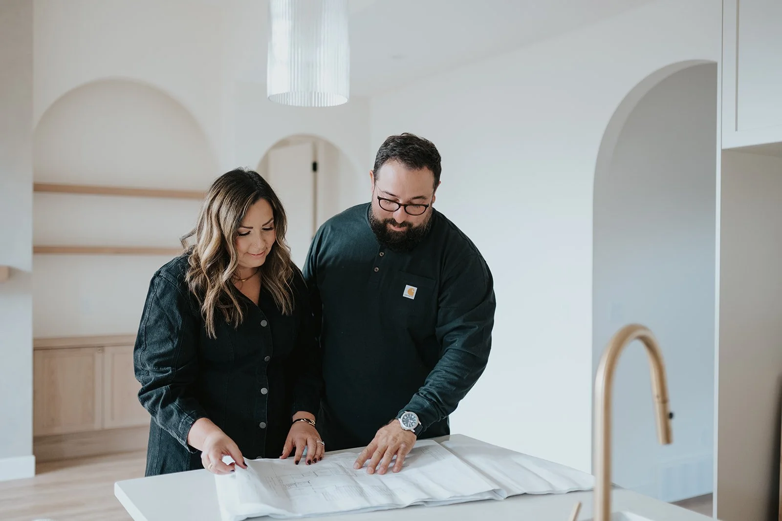 Two people, a man and a woman, looking at architectural blueprints on a white kitchen island.