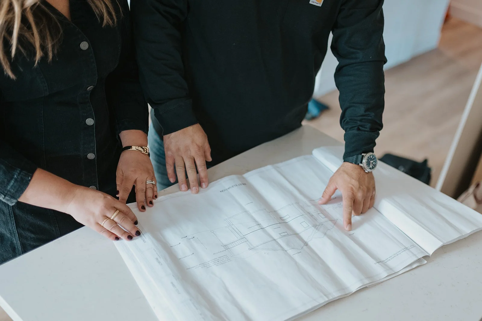 Two people looking at a blueprint on a table, with only their hands and arms visible.