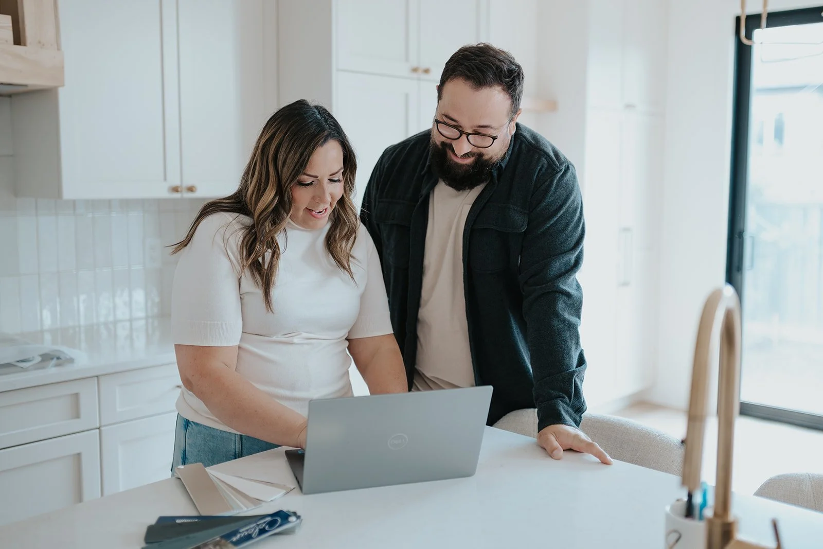 A woman and man looking at a laptop in a bright kitchen.