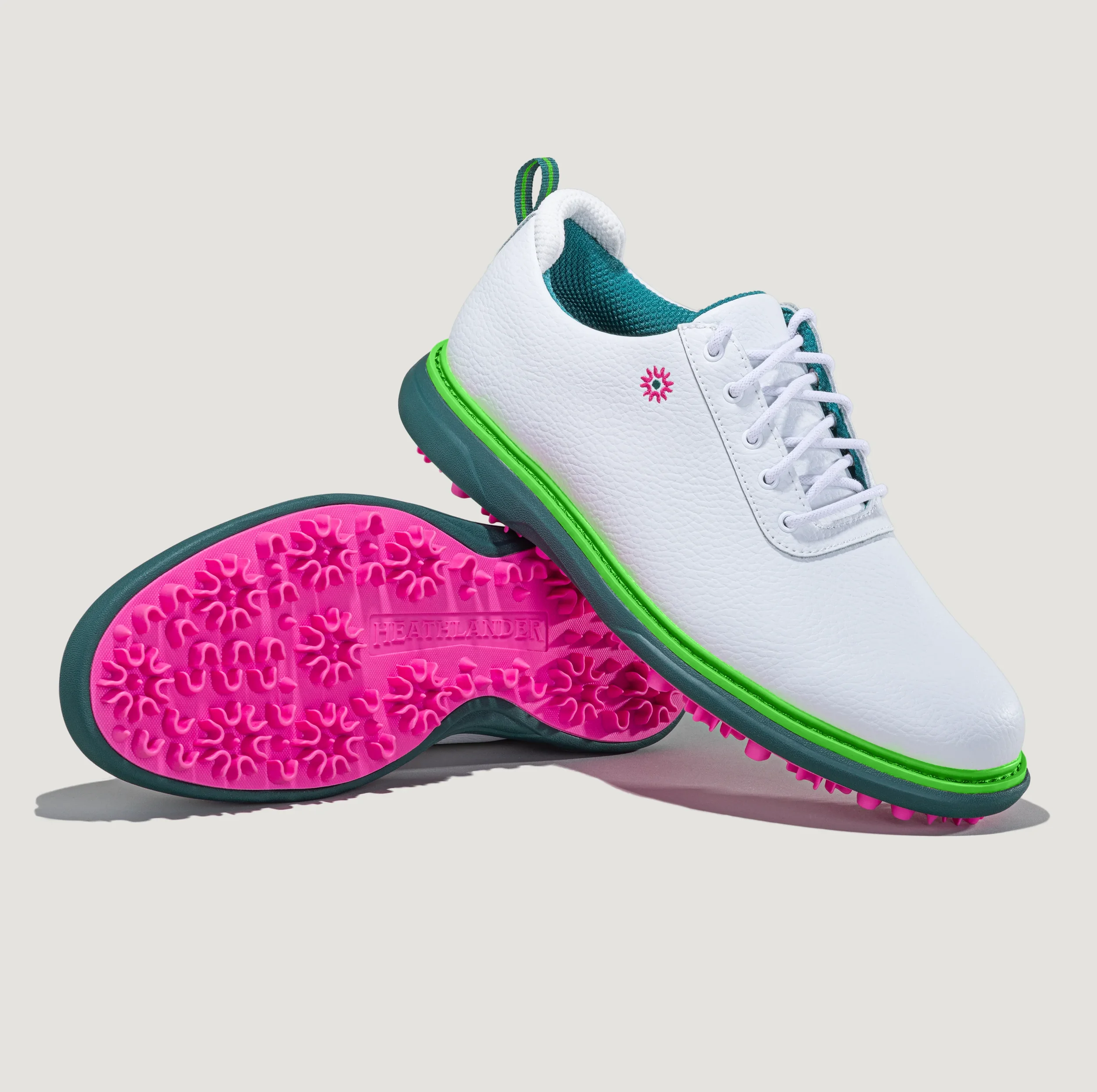 Close-up of a modern and premium white golf shoe with teal accents, a pink logo, and a neon green line on the sole, placed on a pink shoe tread with the brand name 'HEATHLANDER' embossed.