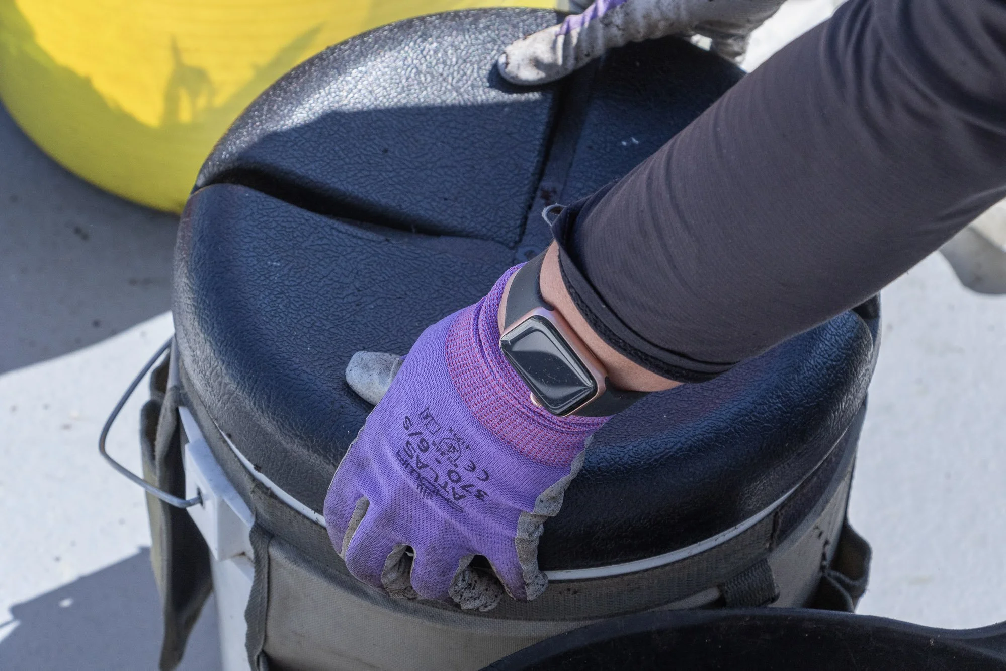A person's arm wearing a fitness tracker and purple glove, resting on a black motorcycle seat with a yellow object nearby.