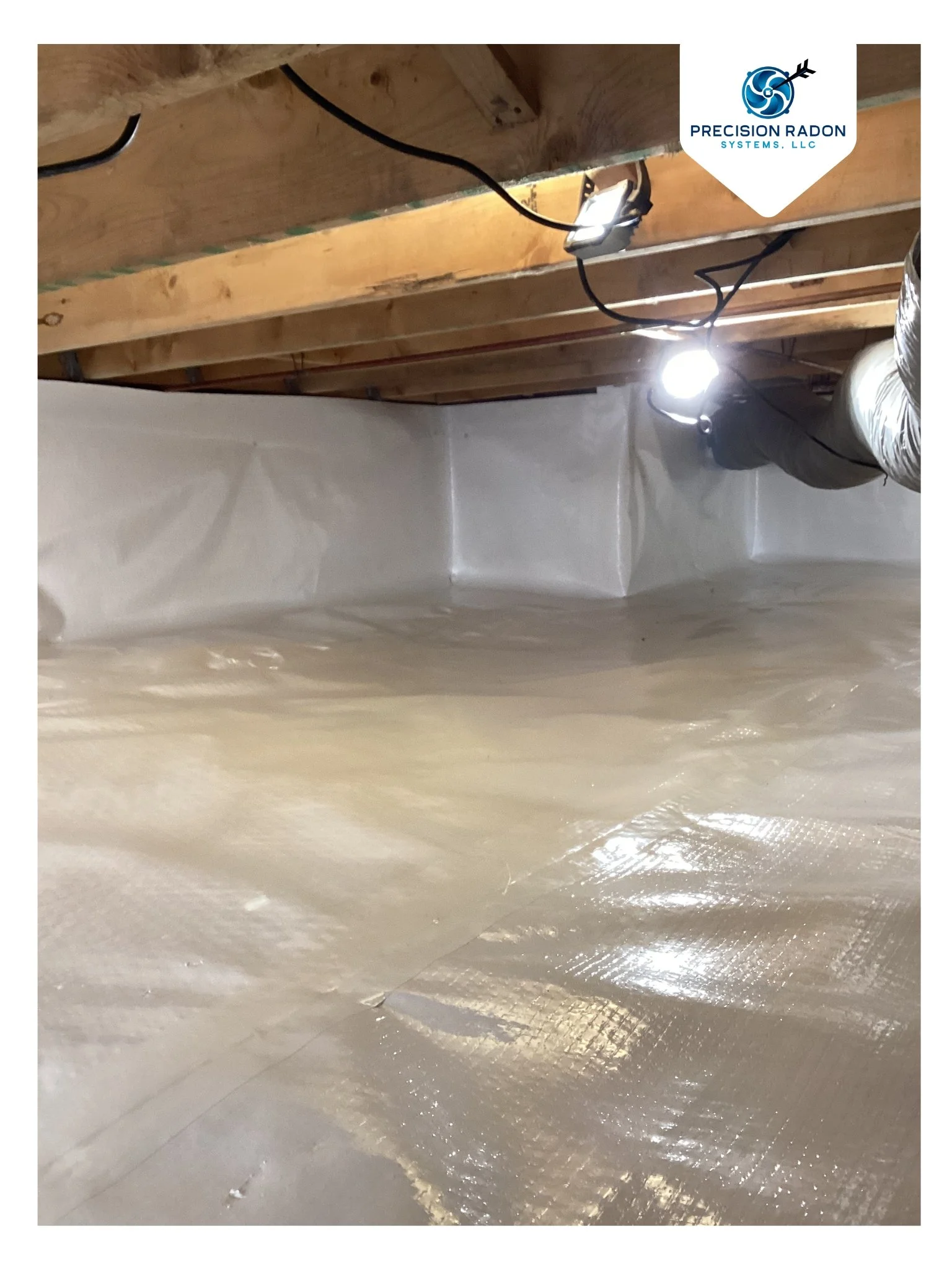 Vapor barrier installed in a crawlspace under a home to help reduce moisture and radon gas. Pictured is the white vapor barrier on the floor and foundation wall, and lights hanging from the top of the crawlspace.