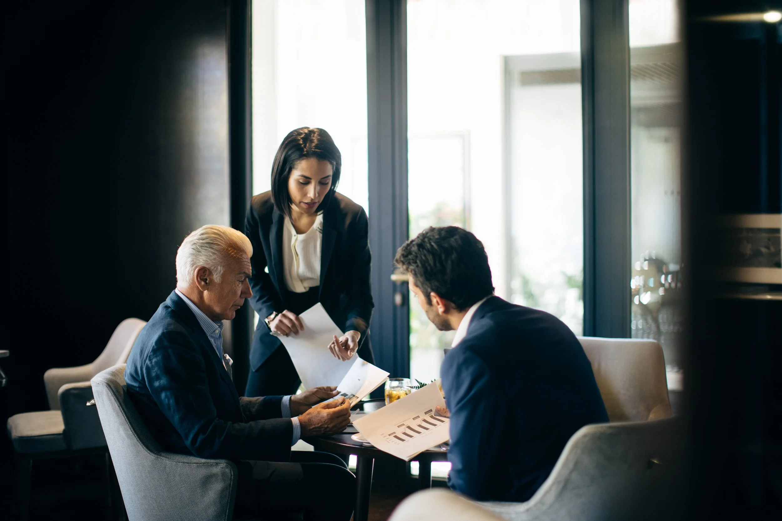 Three business professionals reviewing documents at a meeting in a modern office.