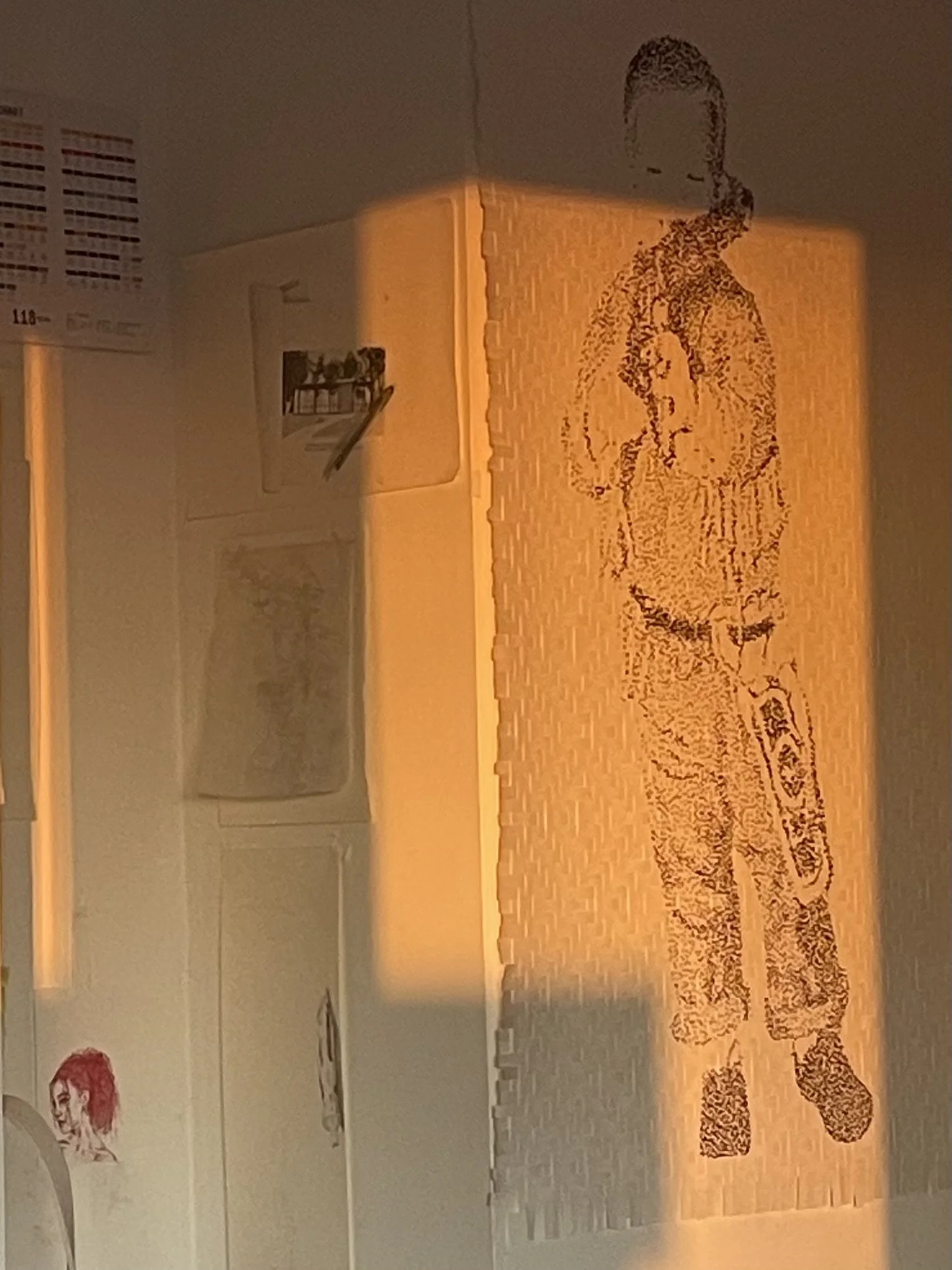 Projection of a woman with her hands in her pockets onto a textured wall, with sketches and paintings visible nearby.