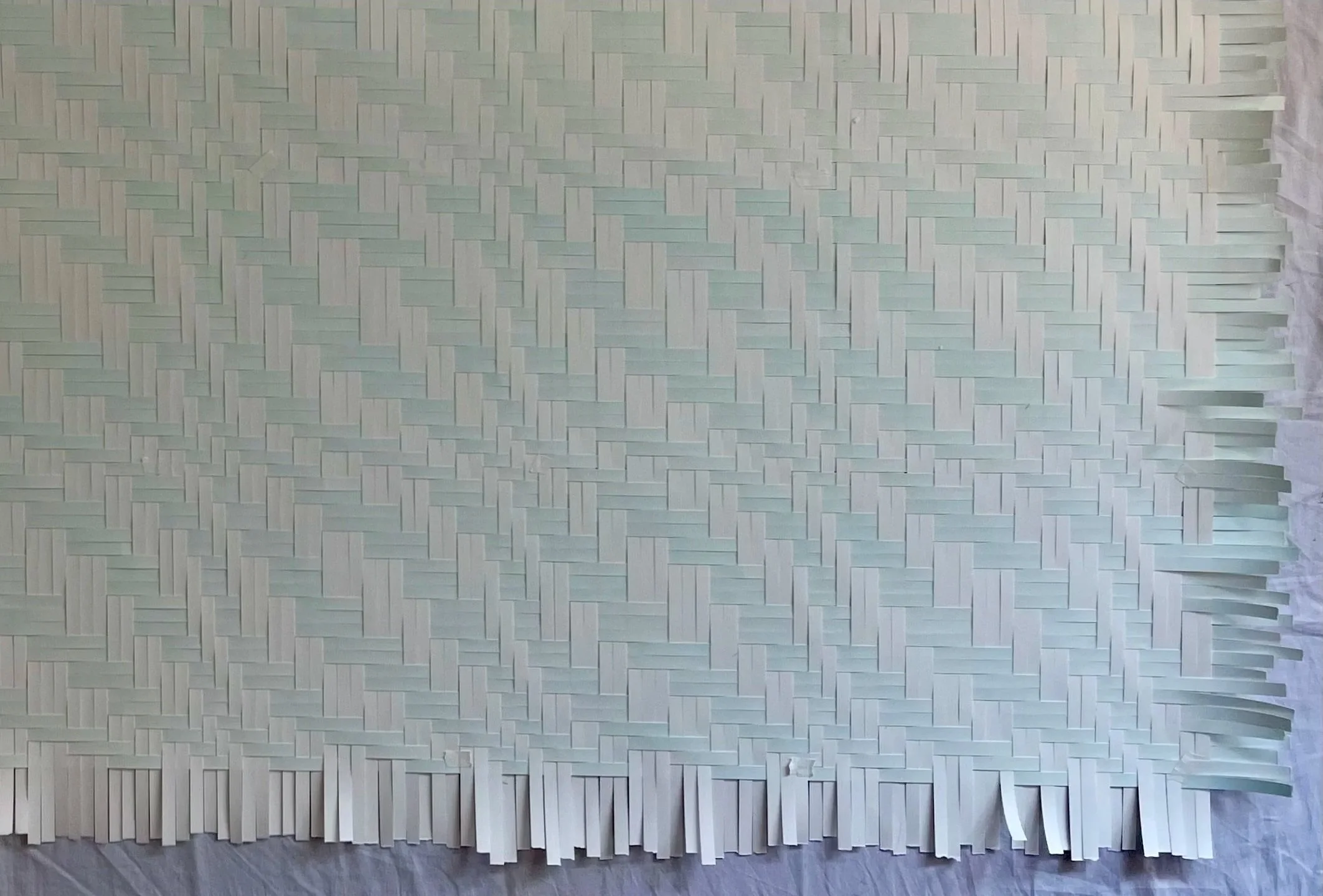 A white textured wall with a woven pattern and fringe at the bottom, possibly made of paper or fabric.