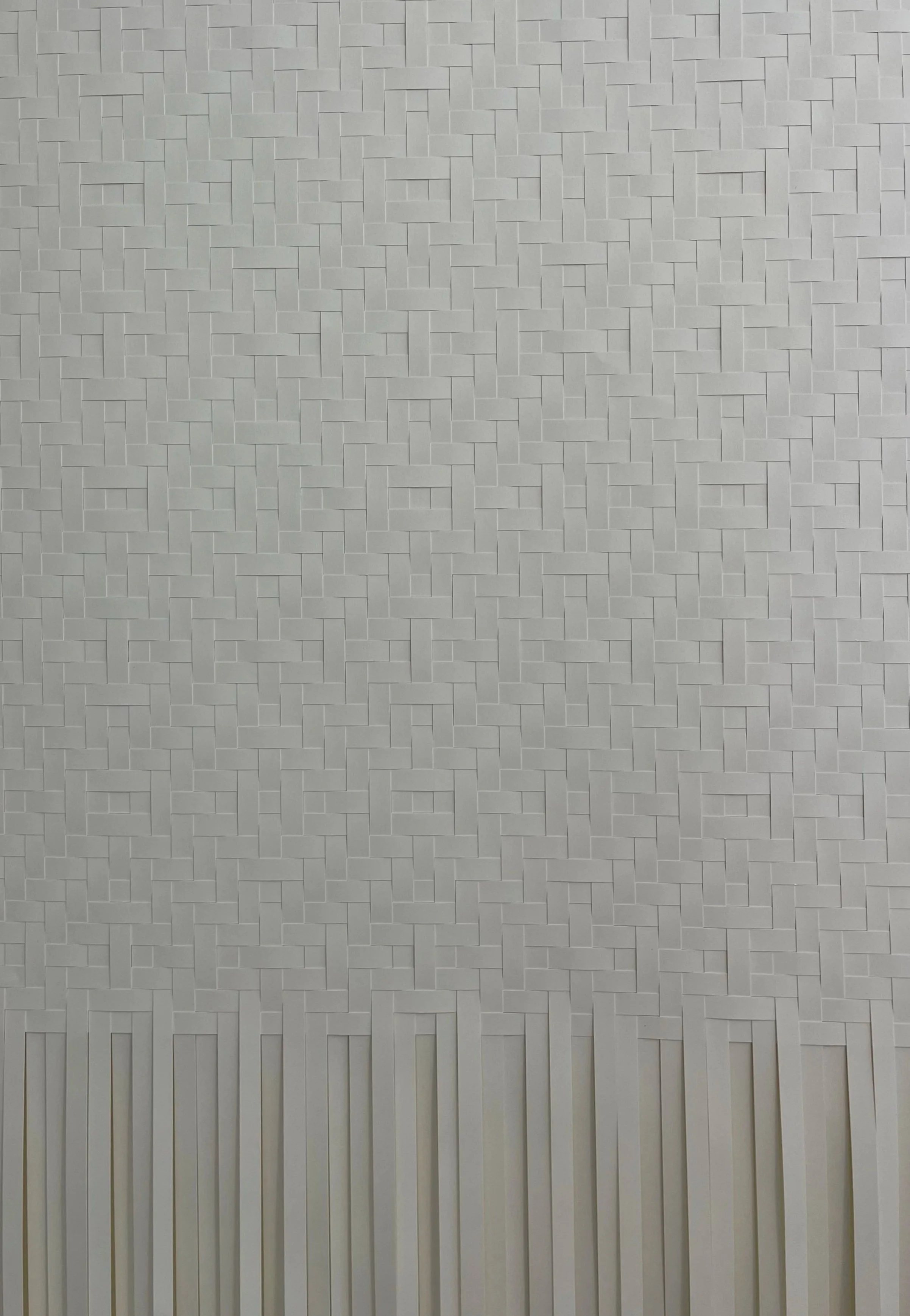 A close-up of a white wall decorated with a pattern of small rectangular tiles arranged in a woven pattern at the top and vertical slats at the bottom.
