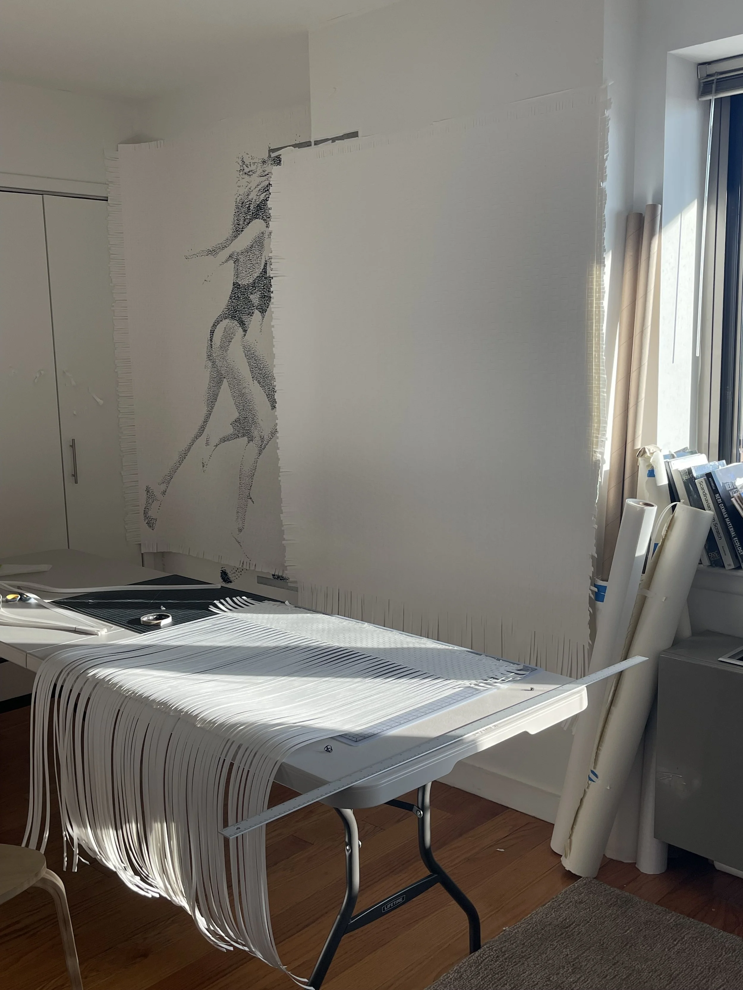 A large art piece of a woman in a swimsuit hanging on a wall, with the quilted backing and fabric strips of the artwork draped over a table below.