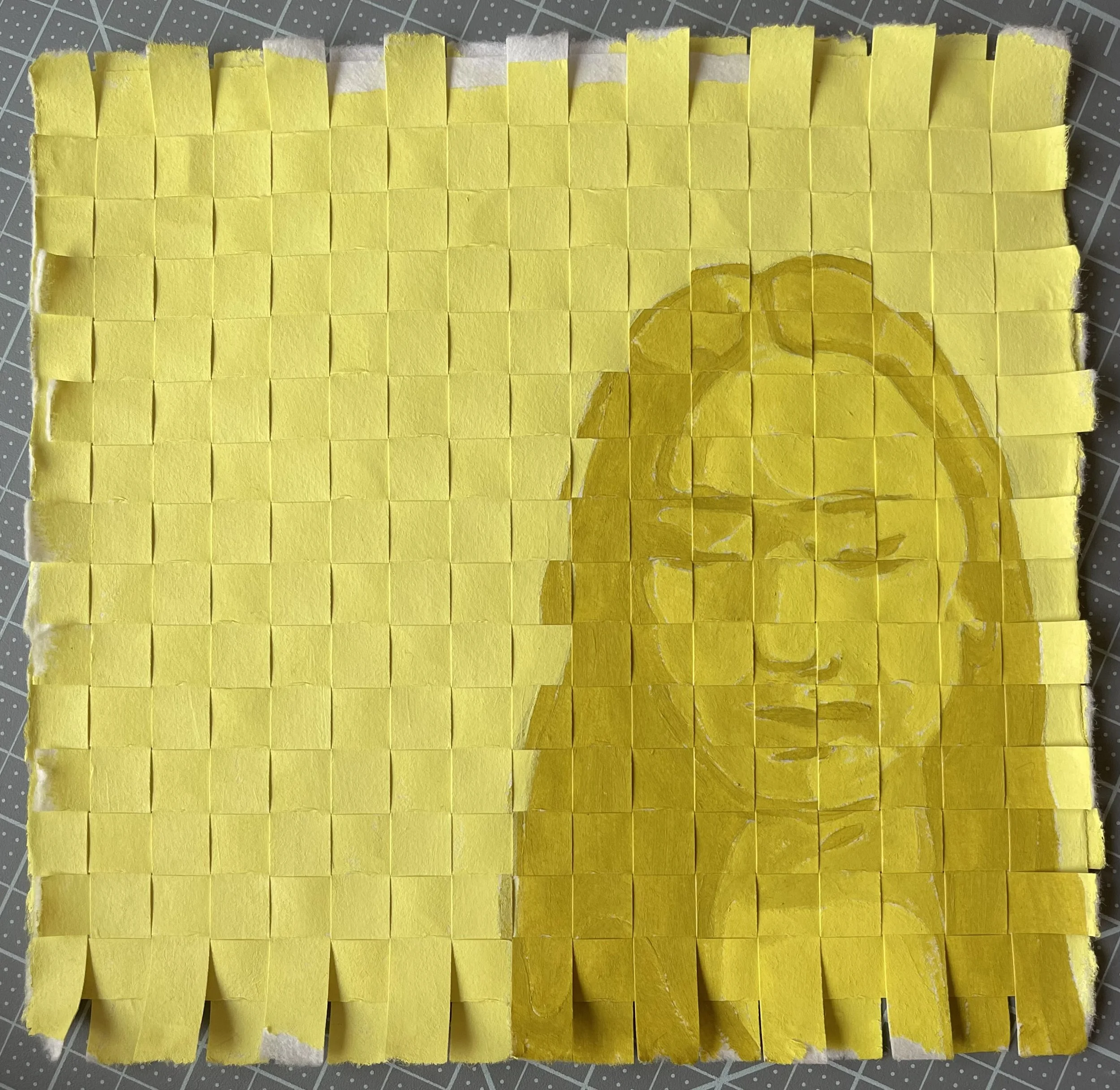 A pixelated yellow paper mosaic with a painted portrait of a woman with glasses, painting on a cutting mat.