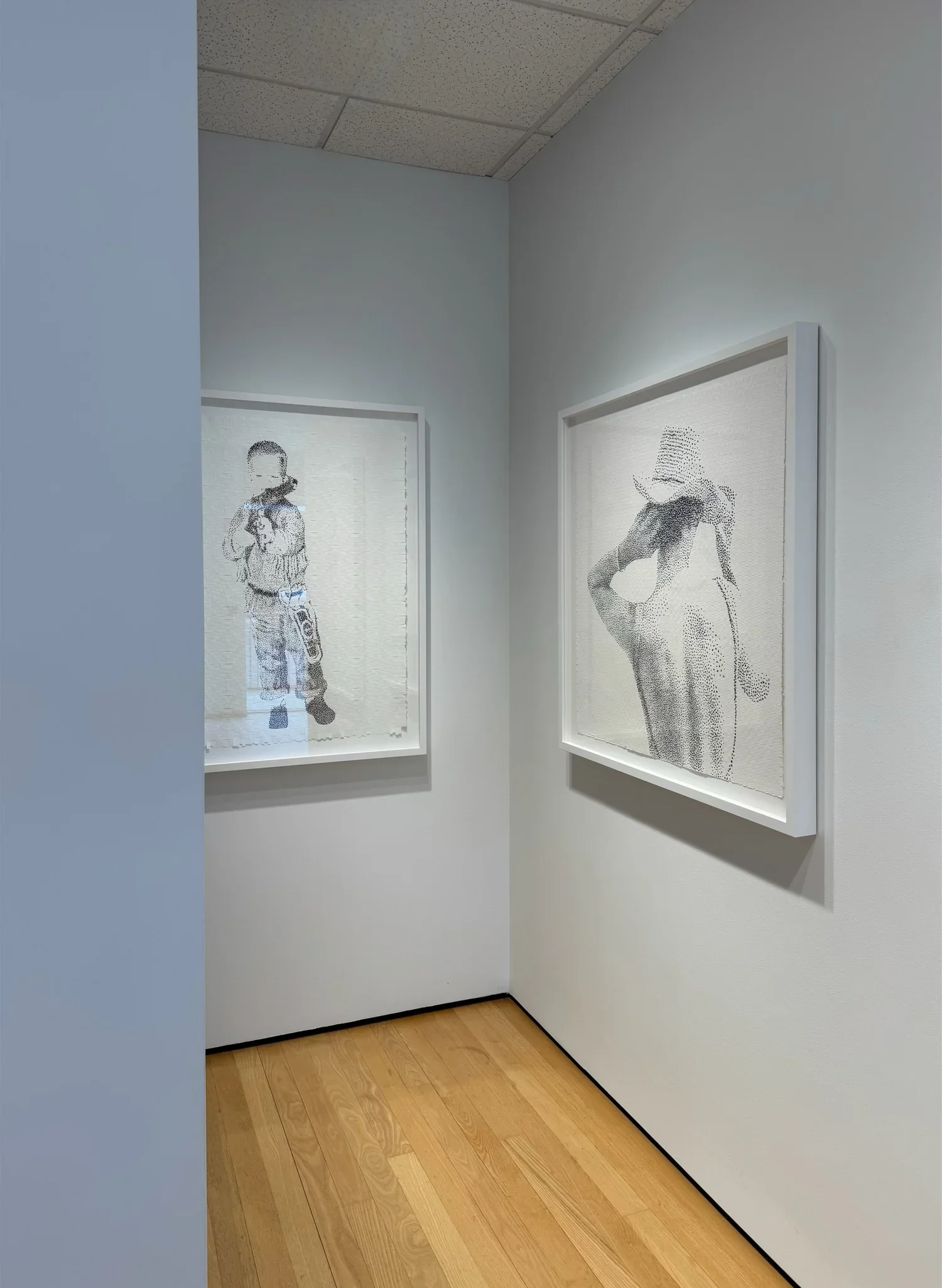 Two framed artworks on a white gallery wall; the left artwork depicts a young boy holding a toy or object, the right artwork depicts a woman with a striped hat and a hand on her hip.
