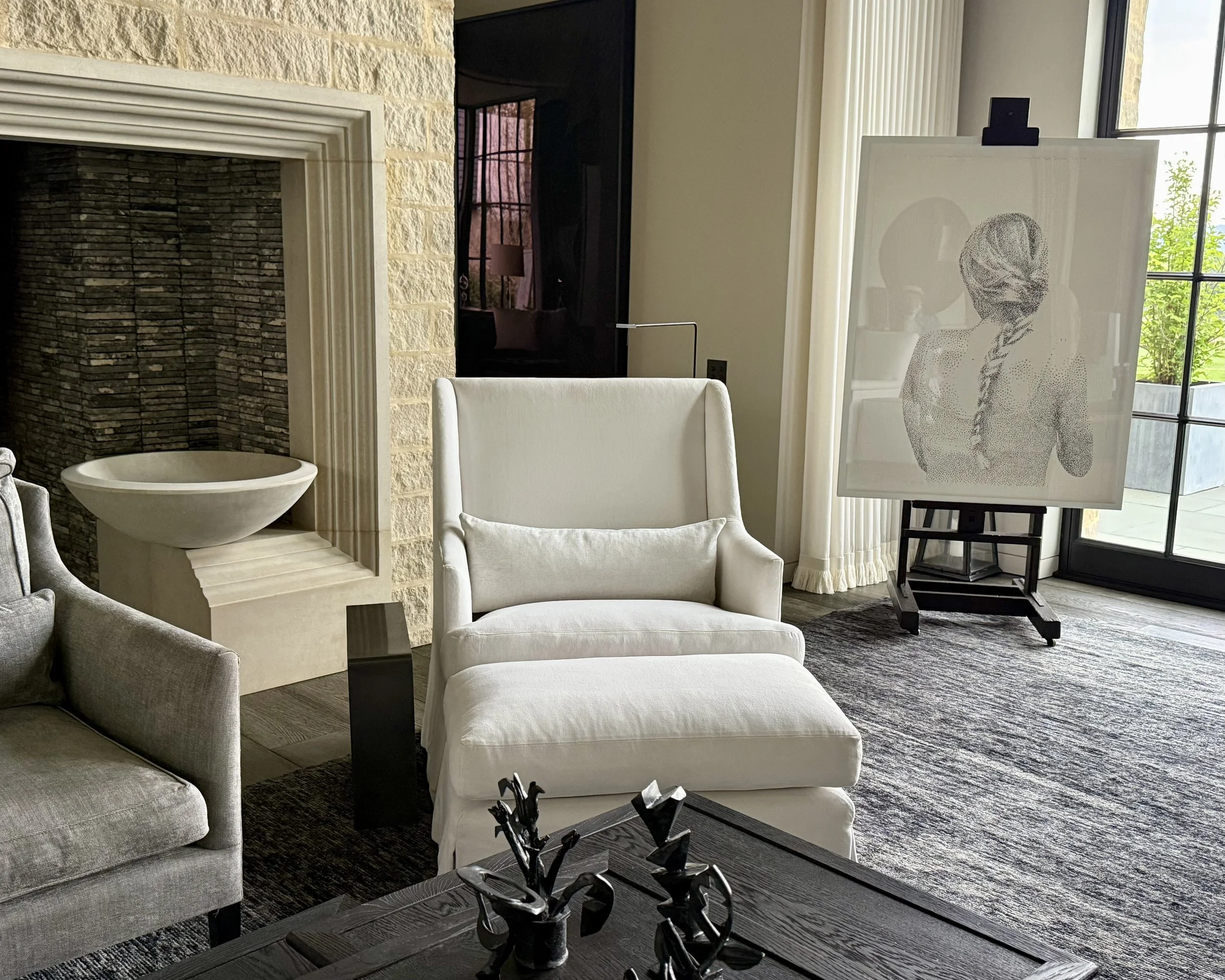 Living room with beige and white furniture, artwork on easel, and a window with curtains.