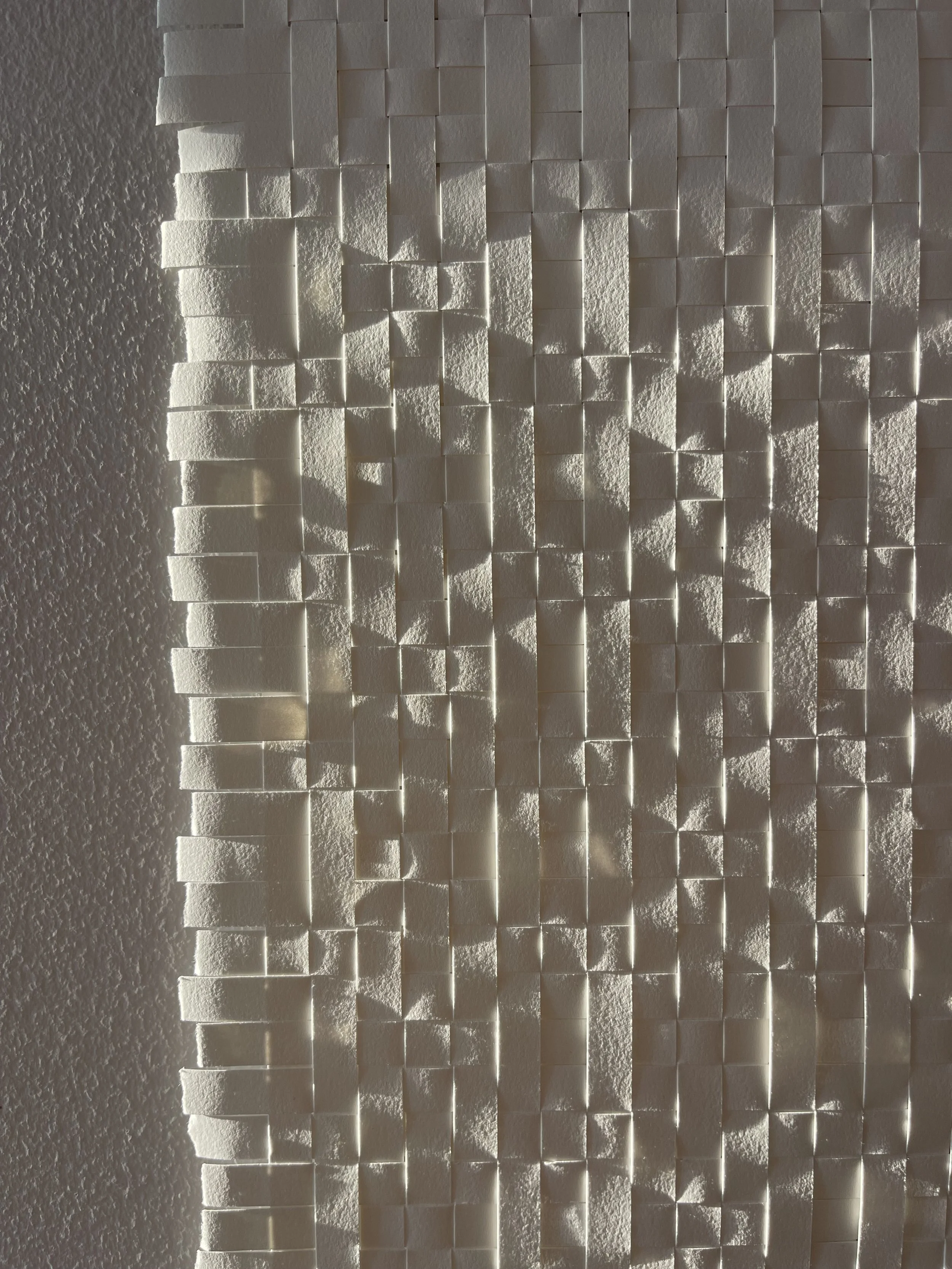Close-up of a textured white wall with 3D rectangular tiles reflecting light.