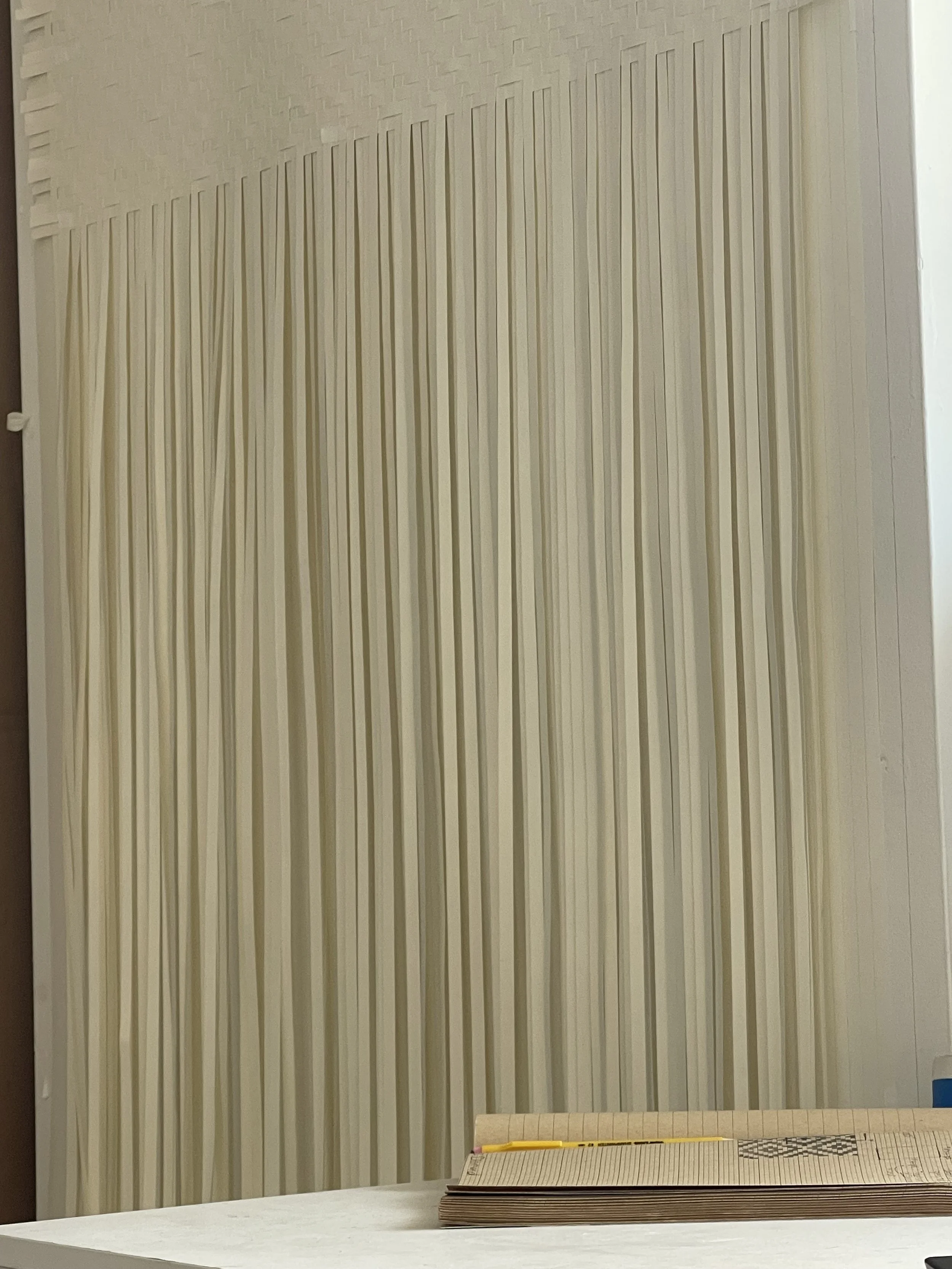 Interior wall with vertical beige acoustic panels and a white table with a closed cardboard box and a yellow pencil.