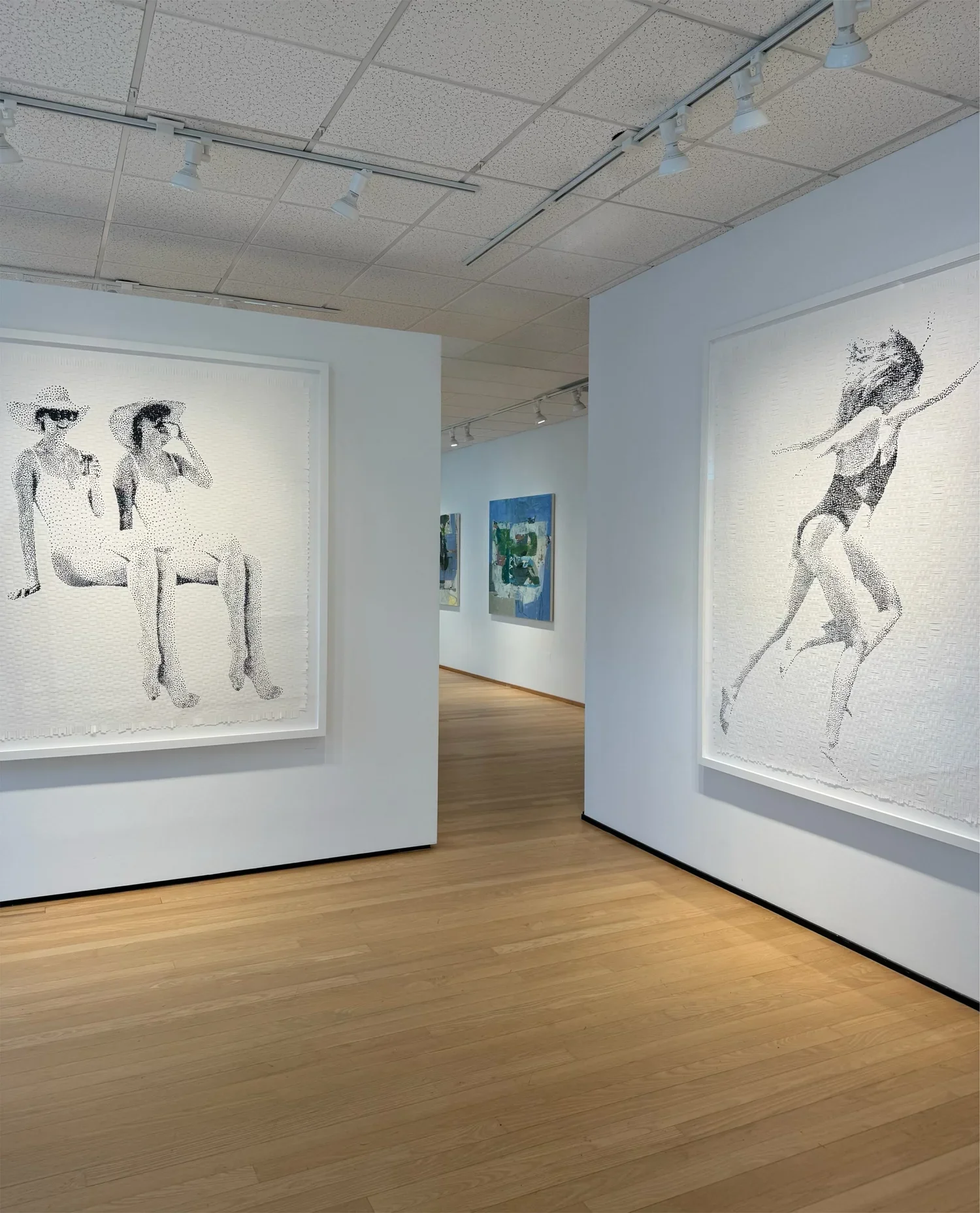 Art gallery with large framed black-and-white photographs of women in summer clothing. The gallery has white walls, a wooden floor, and ceiling track lighting.