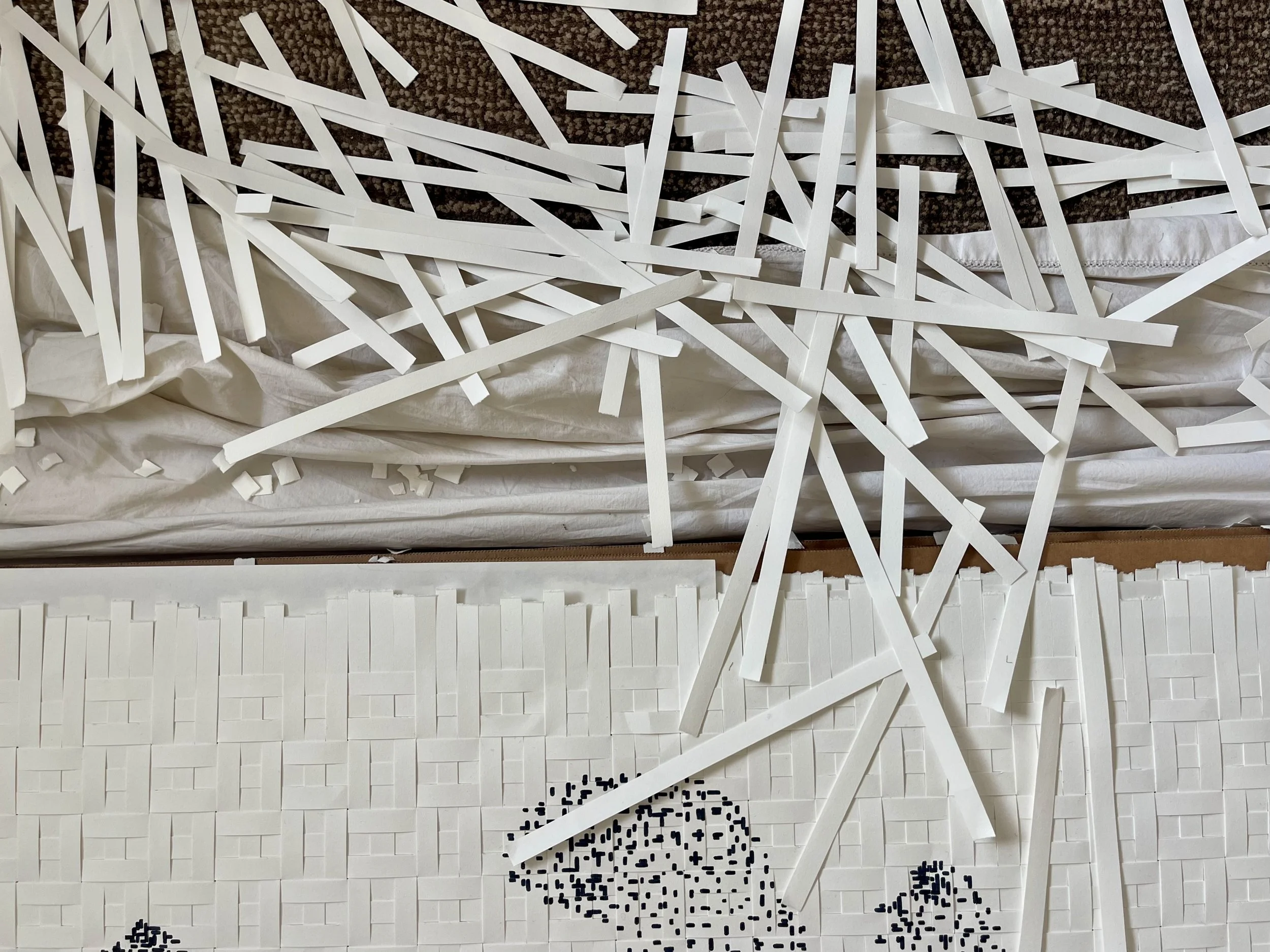 White paper strips and small black squares arranged on white grid paper, with torn paper and scattered strips on top.