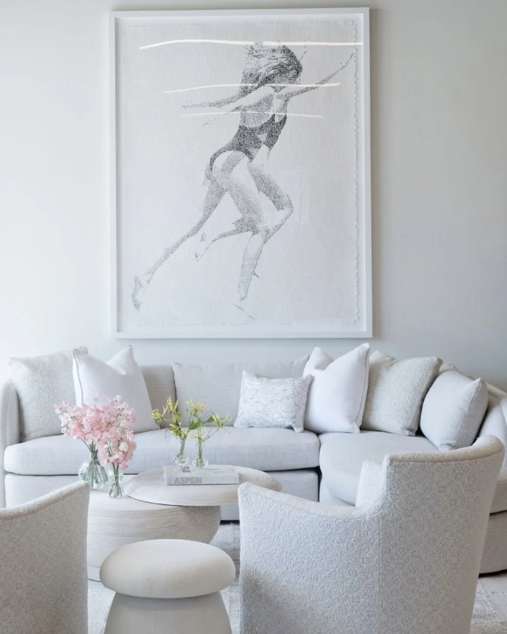 Living room with white sofa, armchairs, and a coffee table decorated with pink flowers. Large artwork of a woman in a swimsuit on a white wall.