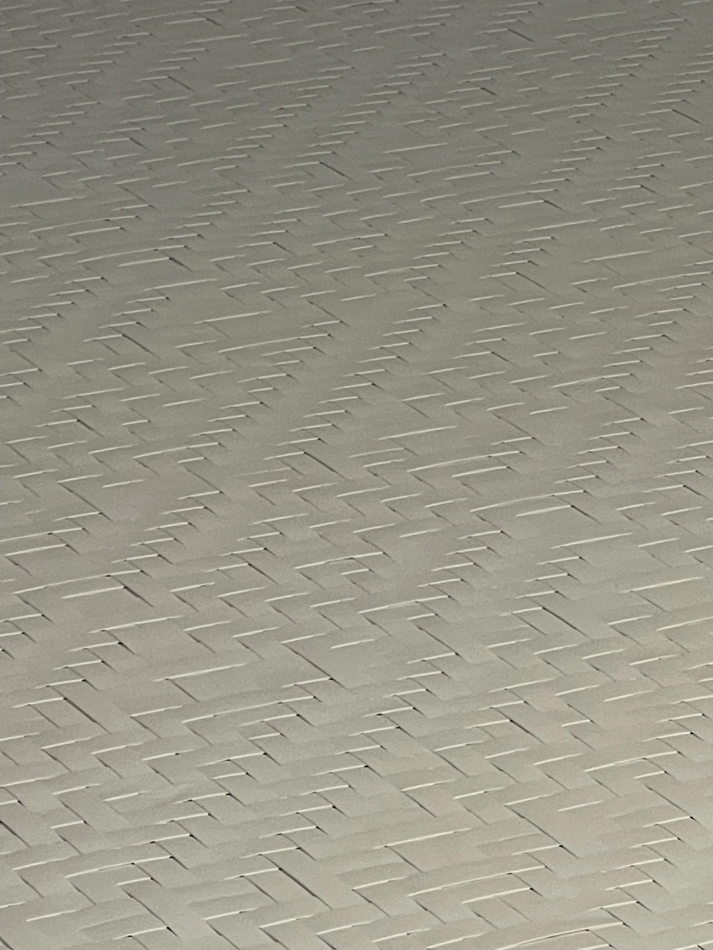 Close-up of a light-colored brick or tile wall with a repeating pattern of rectangular bricks arranged in a herringbone pattern.