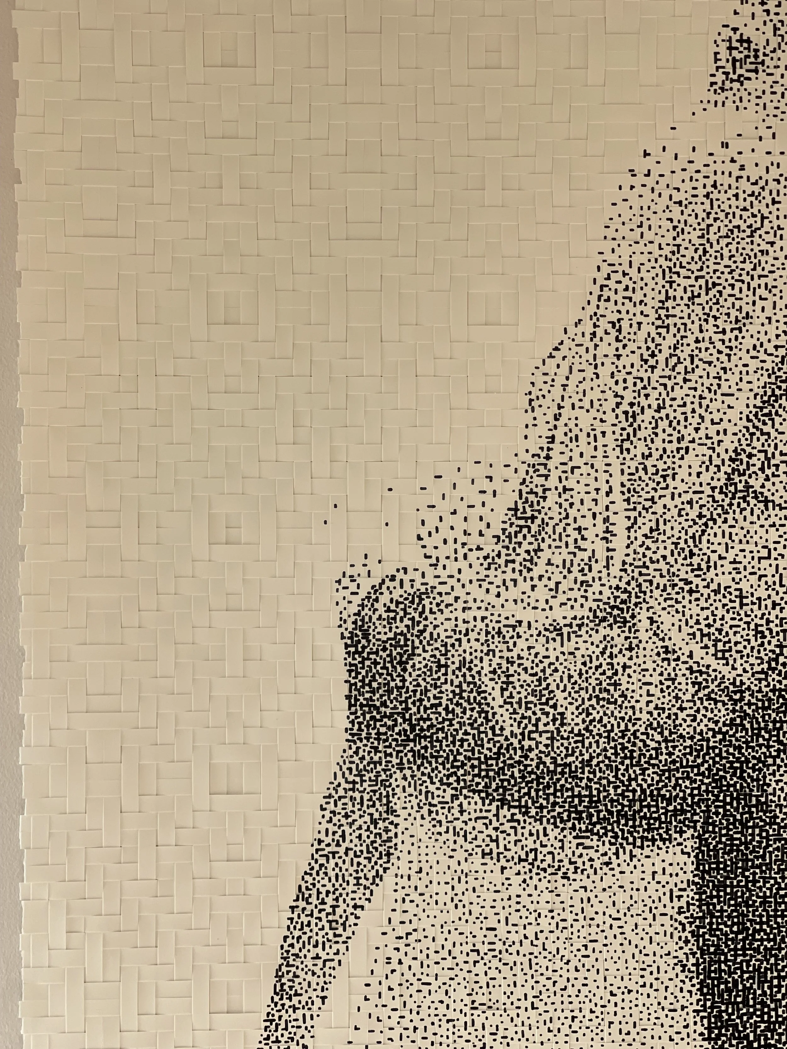 A large wall art piece of a woman's face created from small black square tiles, with a beige tiled background.