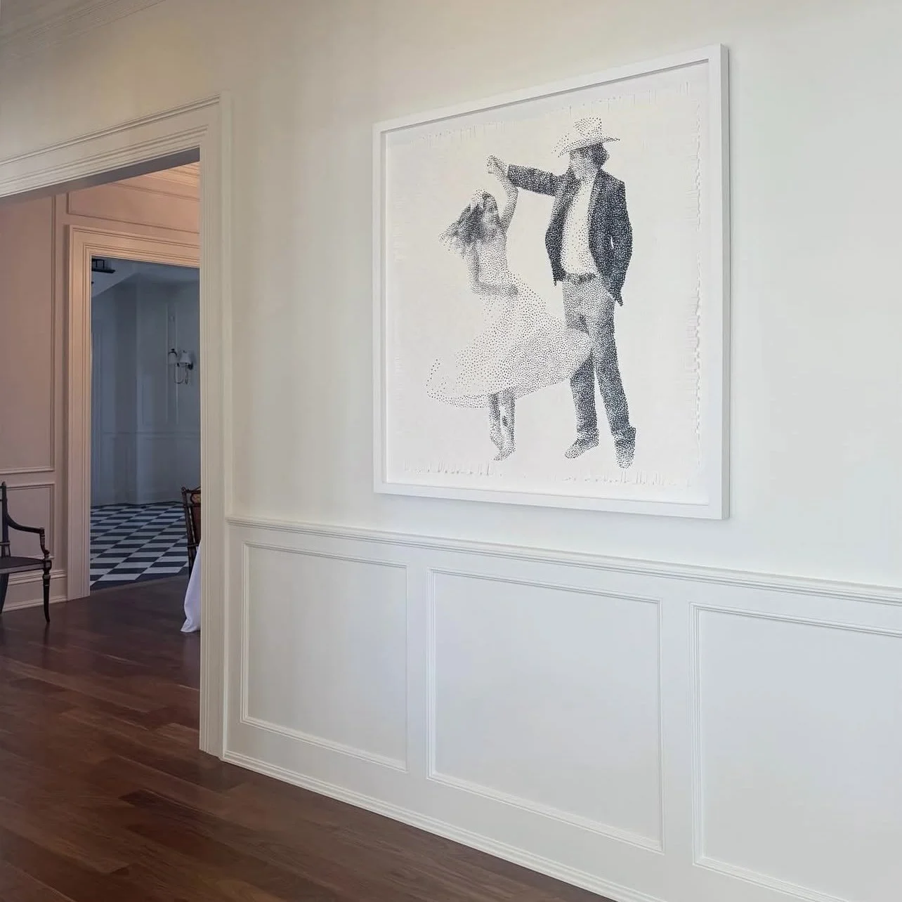 Interior hallway with a white framed artwork on the wall showing a man and a young girl dancing, man wearing a hat and suit, girl in a dress