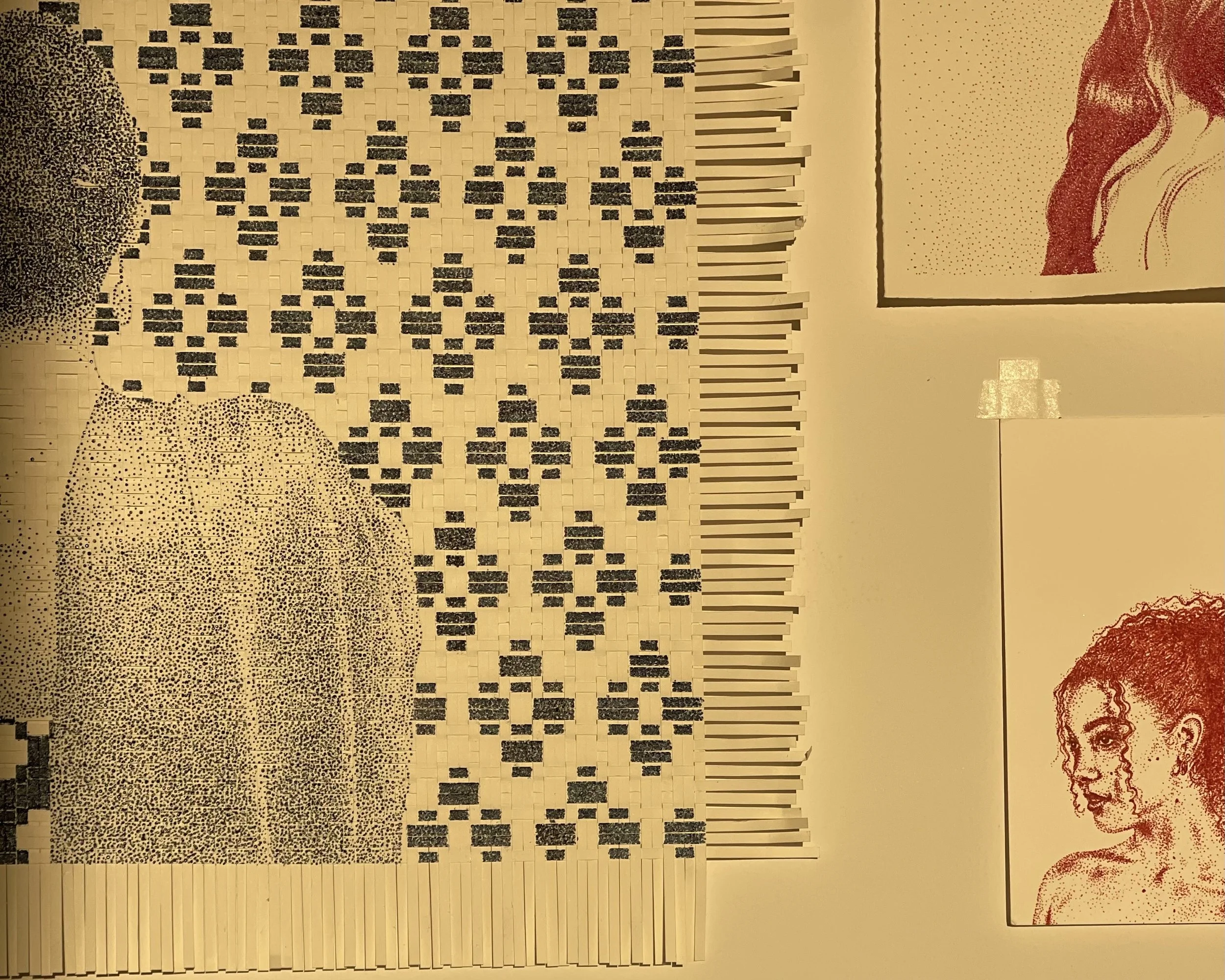 A large artwork made of arranged matchsticks and small black tiles depicting an abstract woman with curly hair, in front of a background with small black dots and rectangular tiles. Two framed portraits of women are on the wall to the right.