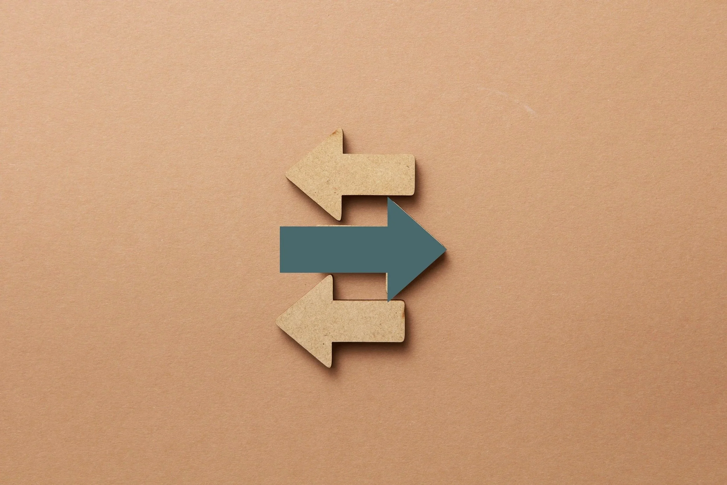 Three cardboard arrows arranged vertically on a beige background, with the top and bottom arrows pointing left and the middle arrow pointing right.