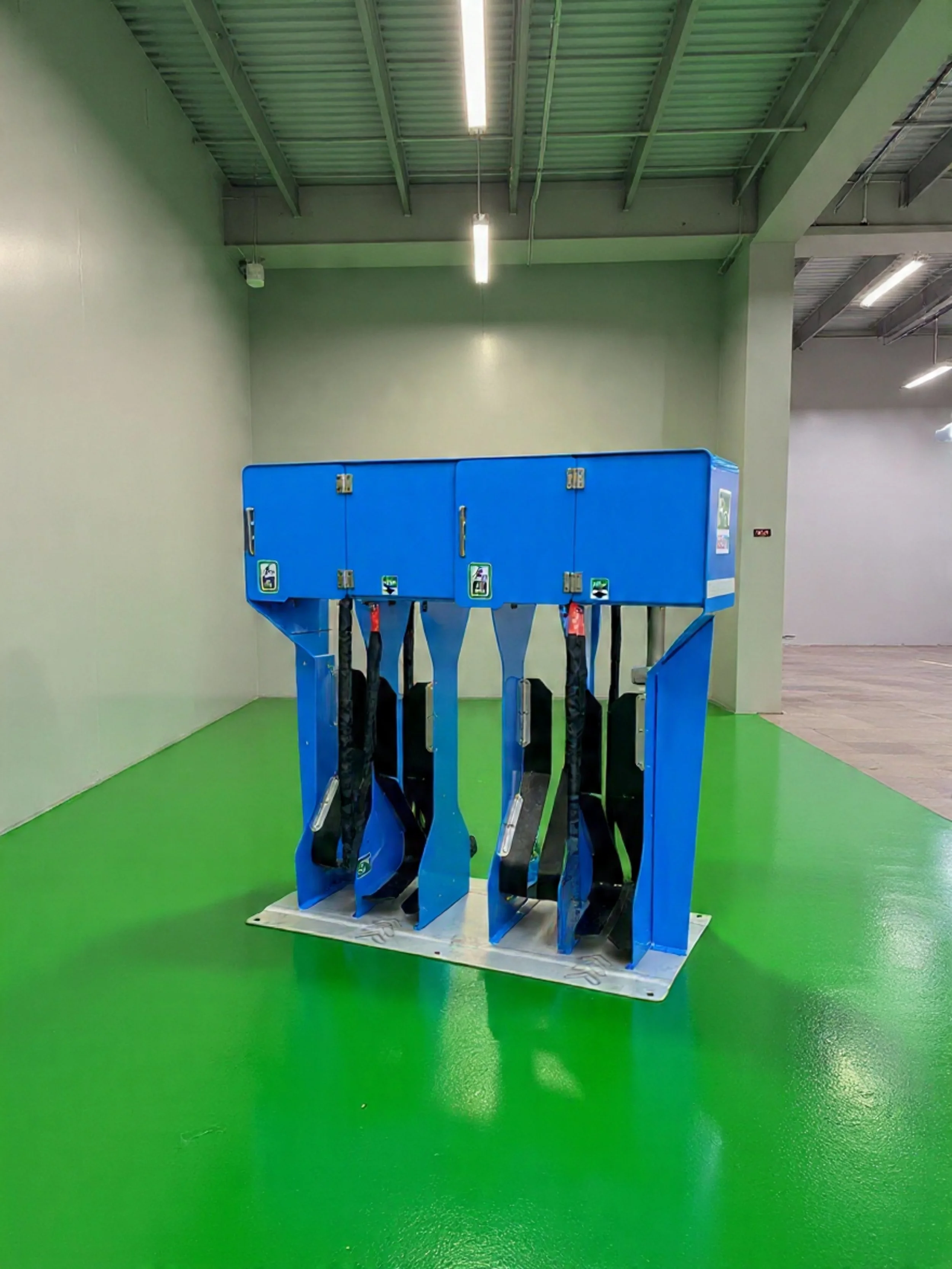 An indoor golf driving range with a blue golf ball dispenser machine on a polished green floor.