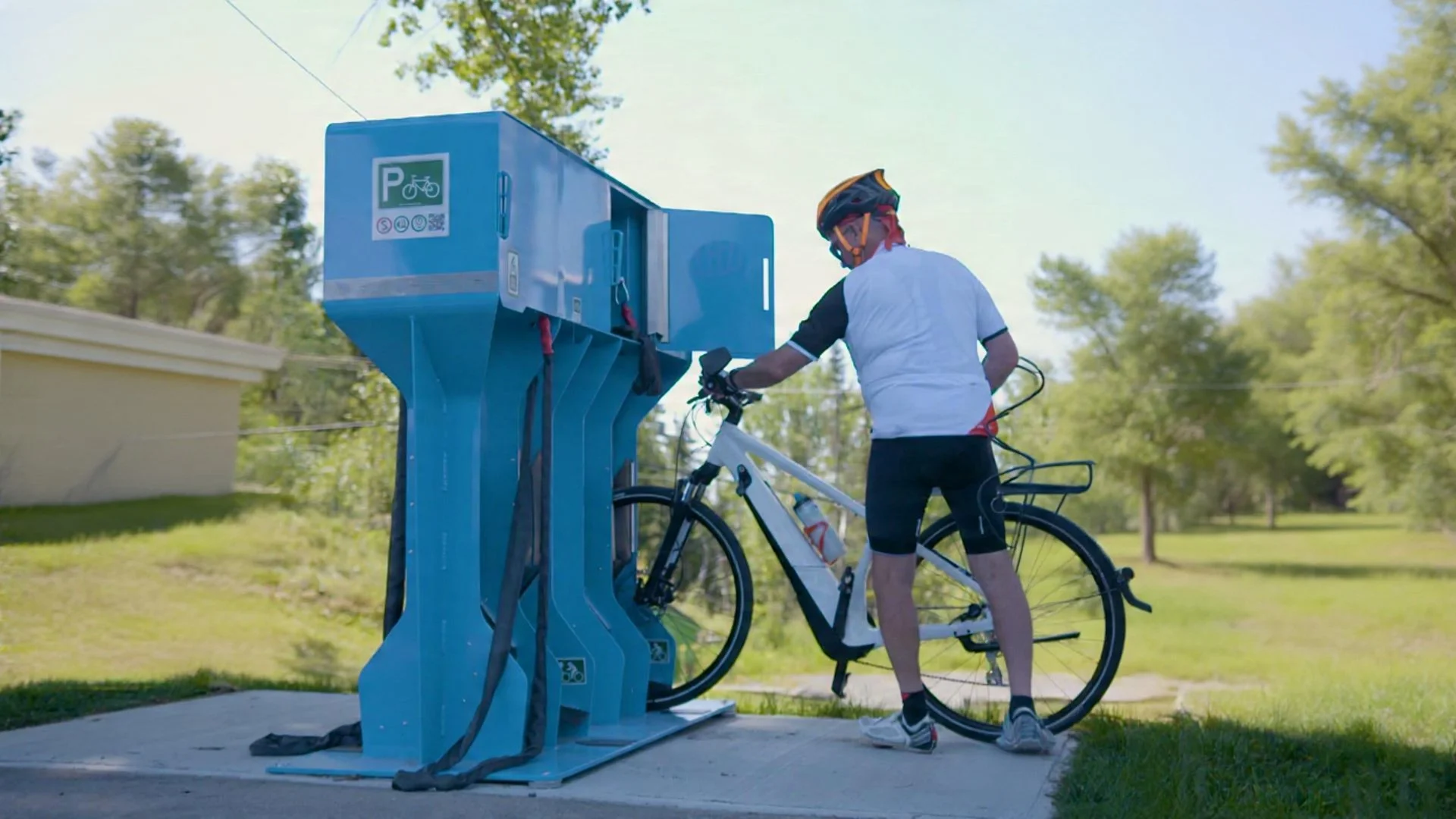 Man with a bicycle using a bike repair station in a park or outdoor area with trees and grass.