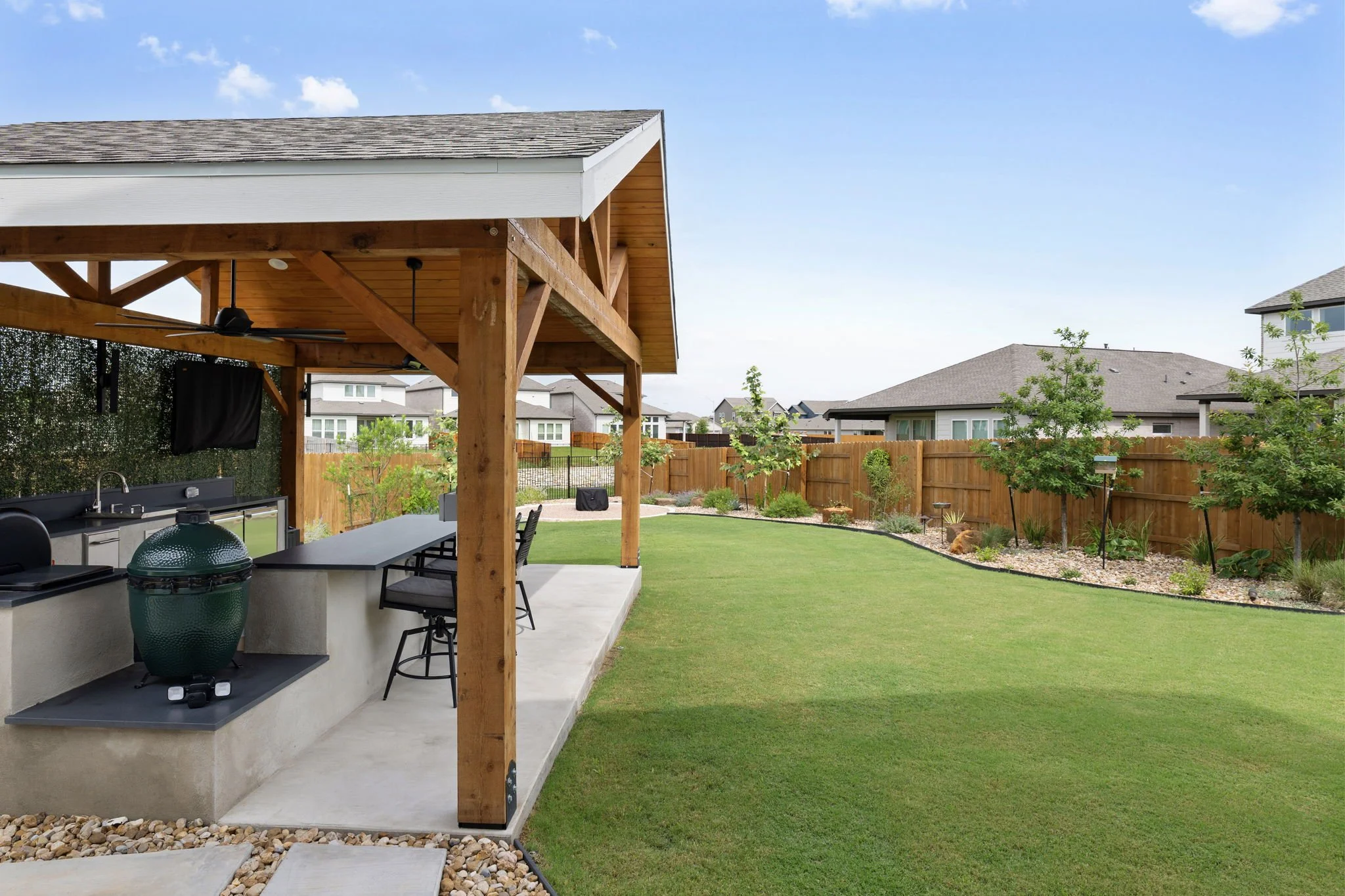 Cedar timber-frame pavilion with built-in outdoor kitchen and bar seating overlooking a sodded backyard