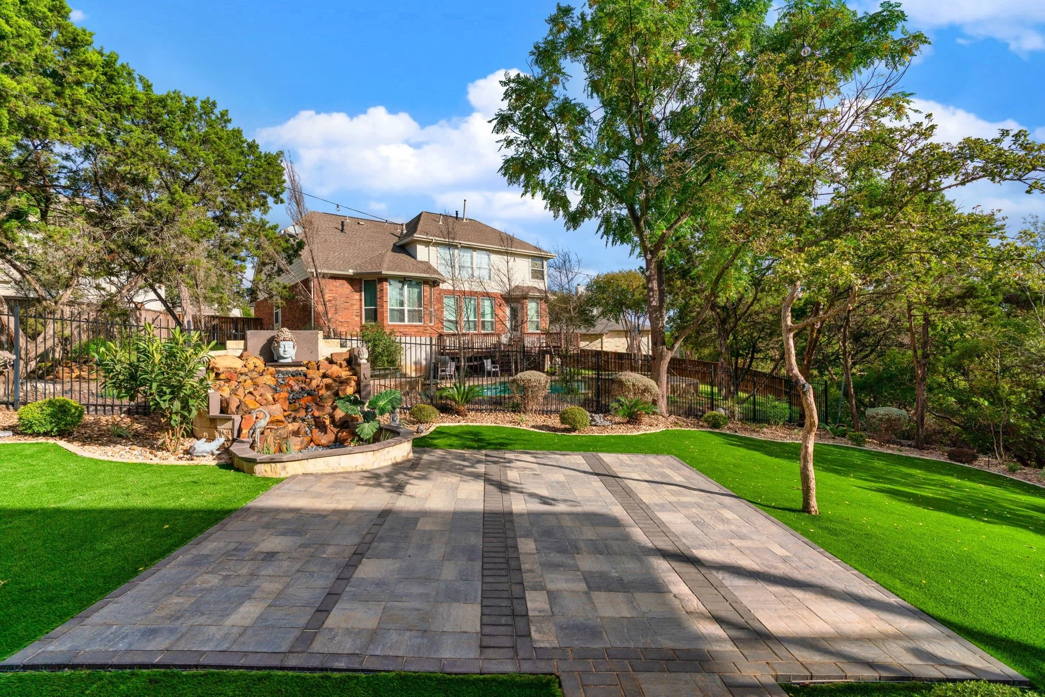 Landscaped backyard with a paver patio, vibrant artificial turf, decorative stone edging, and a cascading water feature.