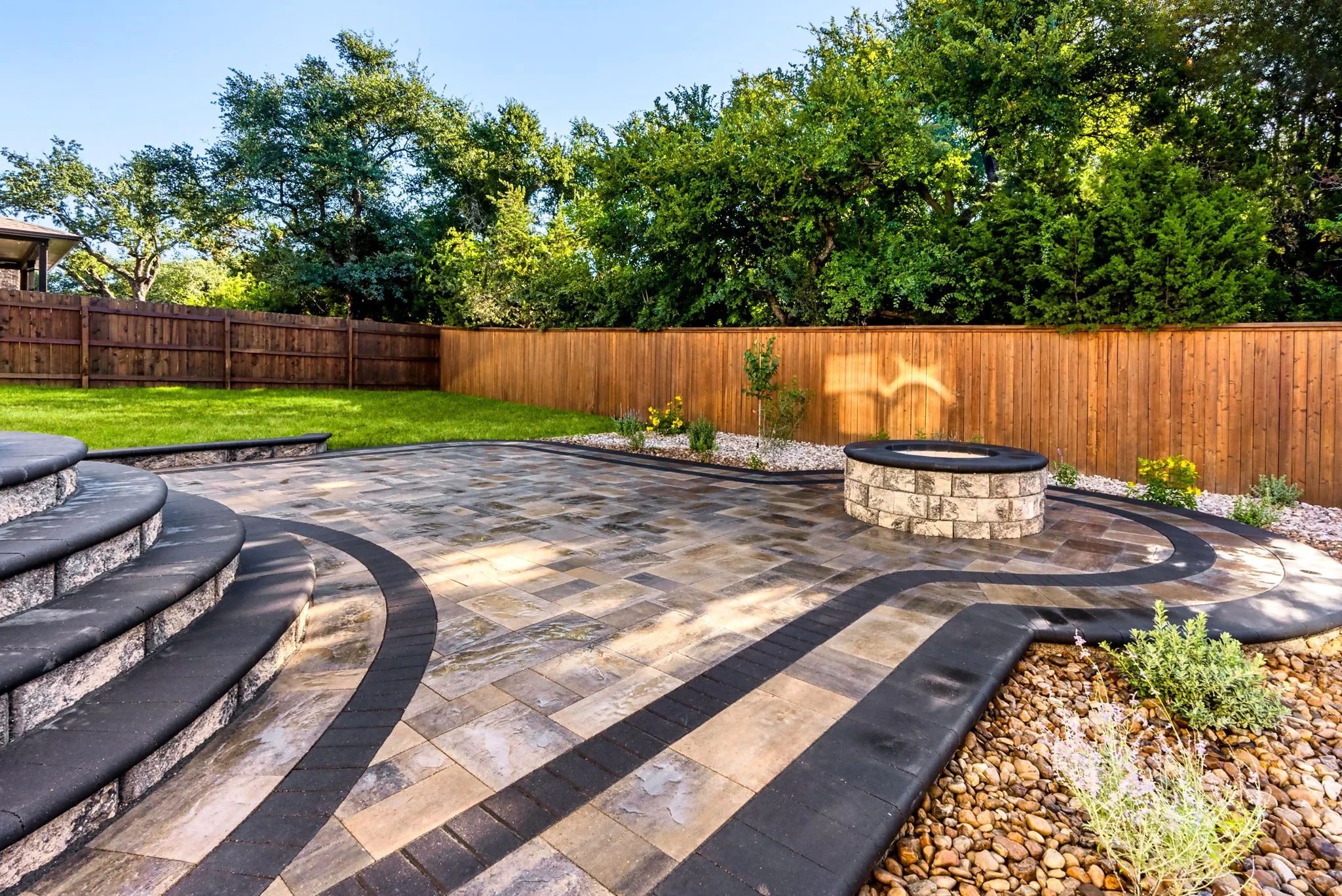 Modern patio with a circular stone fire pit, curved steps, and paver design creating a stylish backyard feature