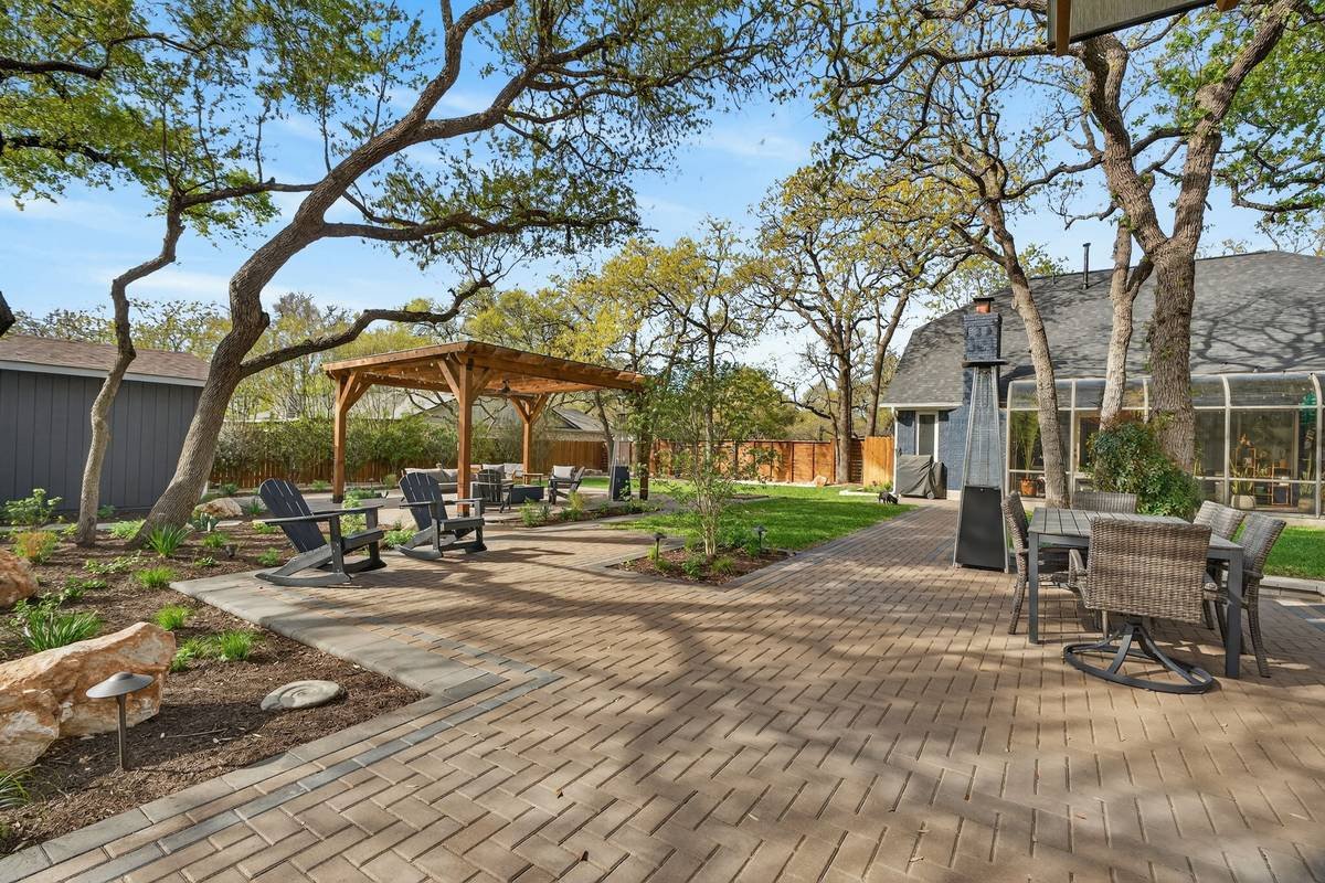 Paver walkway under oak trees with a dining set and cedar pergola beyond — Southern Love Landscaping & Design