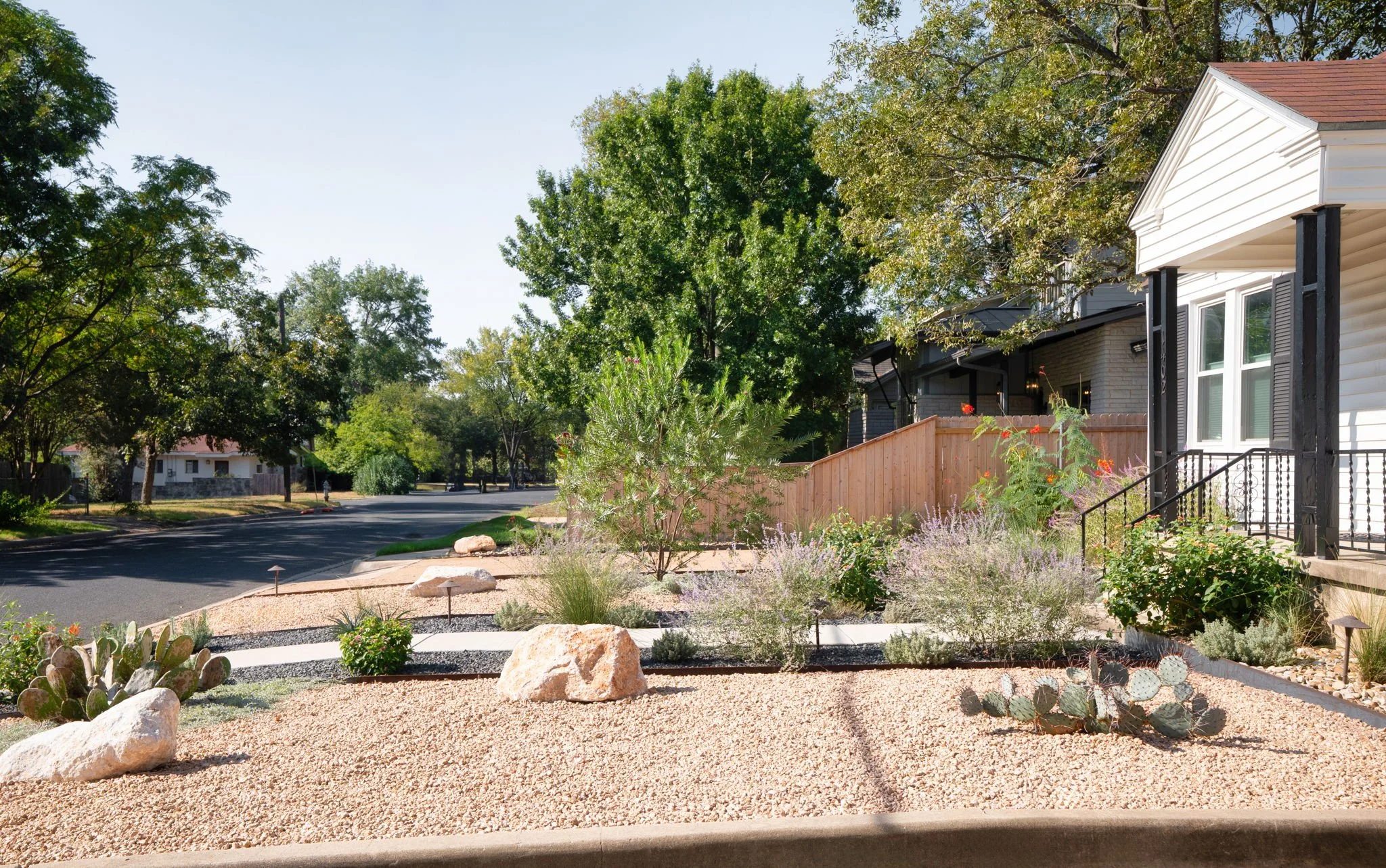 Street-level view of a drought-tolerant front yard with cactus, boulders, and stepping-stone path to the curb