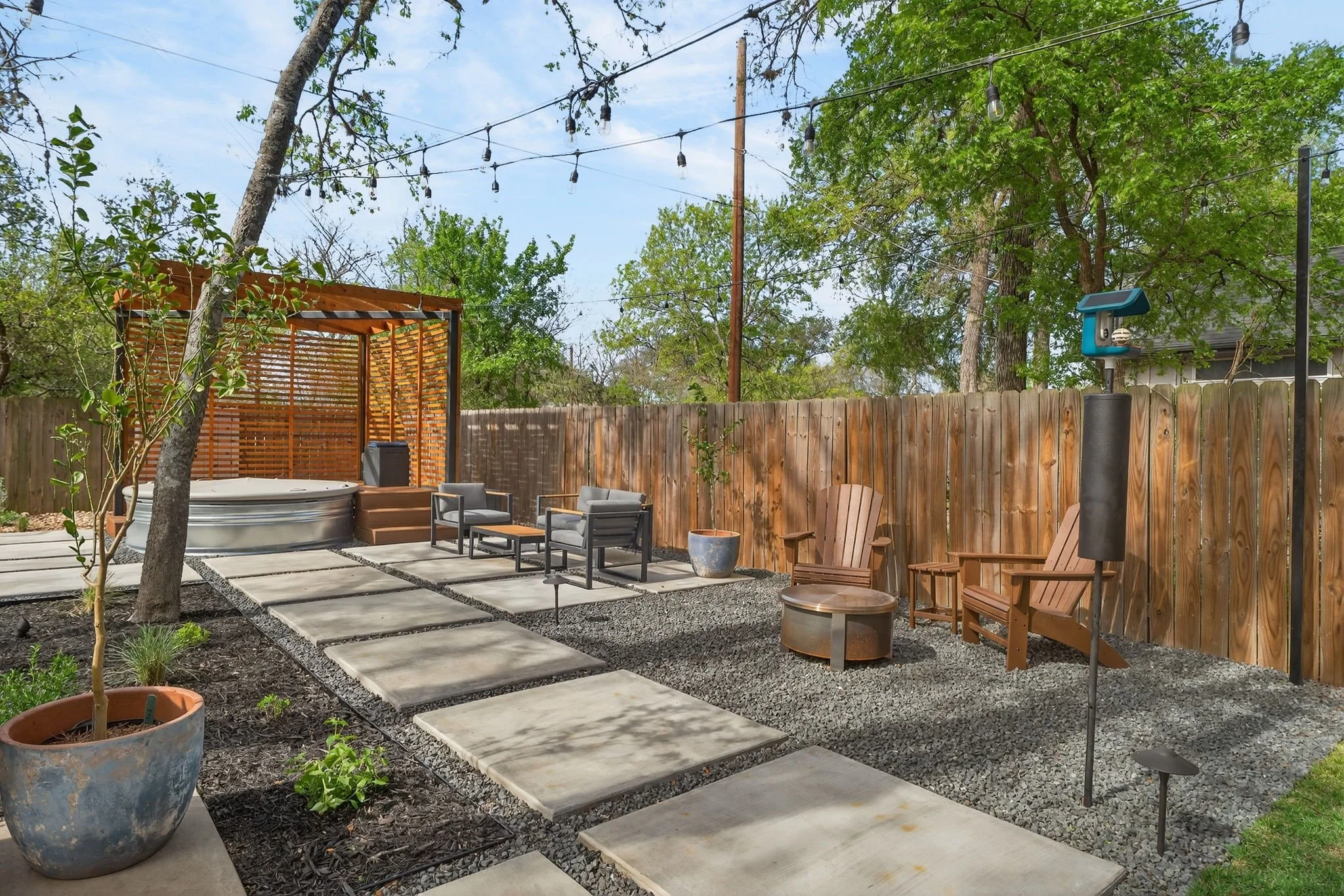 Cedar privacy pergola with stock tank tub, Adirondack chairs, and copper fire bowl on a gravel patio