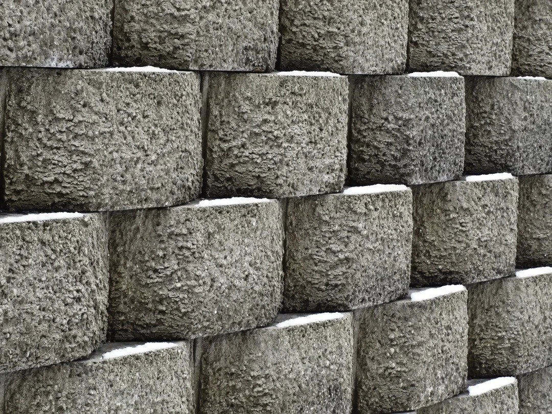 Close-up of interlocking concrete retaining wall blocks with a textured finish, stacked with slight snow in the joints for contrast.