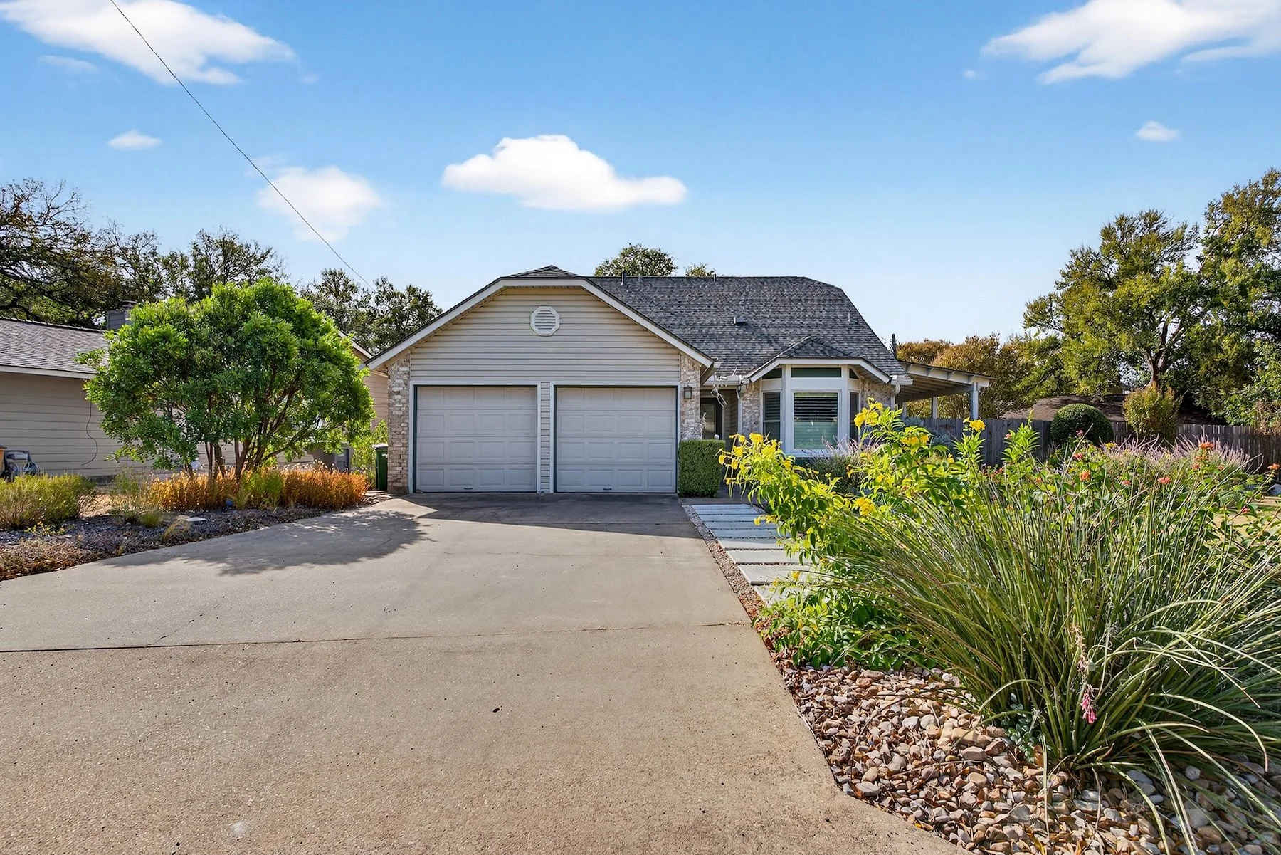 Concrete driveway edged with a river rock border and ornamental grasses beside a two-car garage