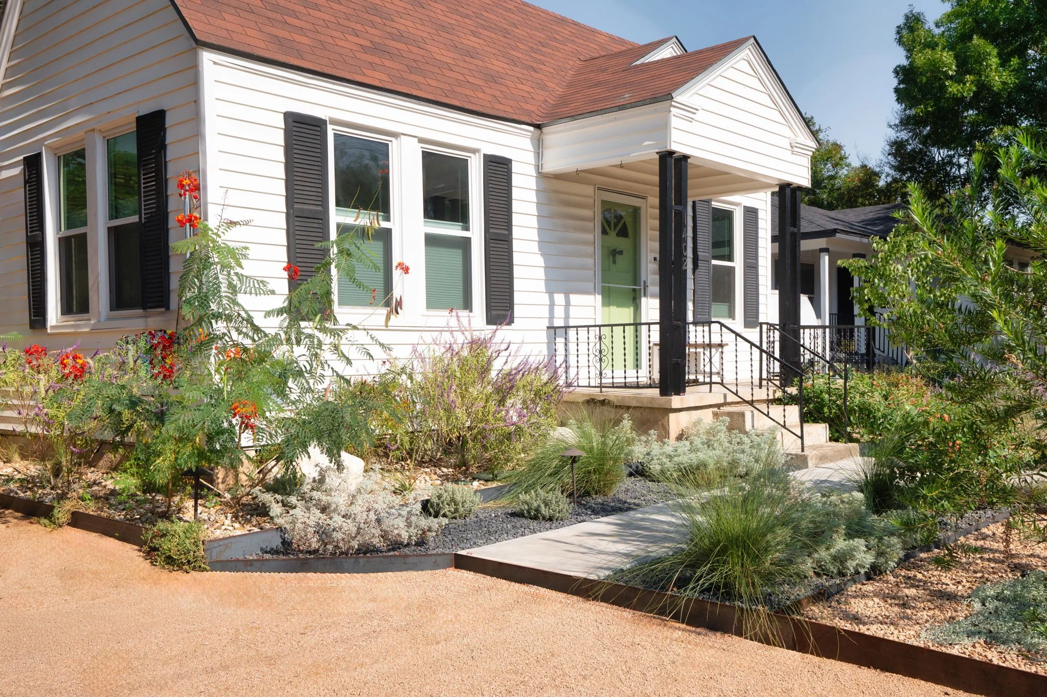 Foundation bed with pride of Barbados, ornamental grasses, and silver-foliage perennials along a covered porch
