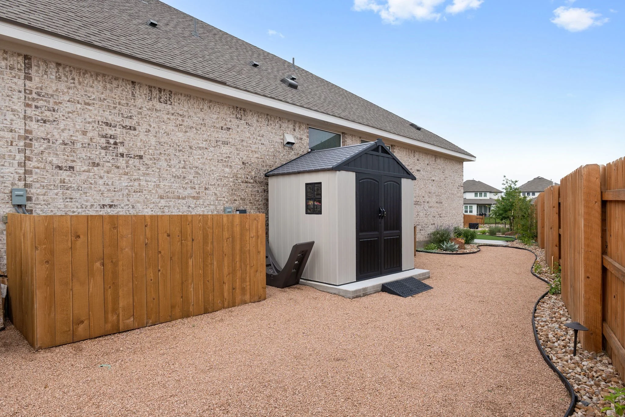 Low-maintenance side yard with decomposed granite ground cover, storage shed pad, and steel-edged river rock border