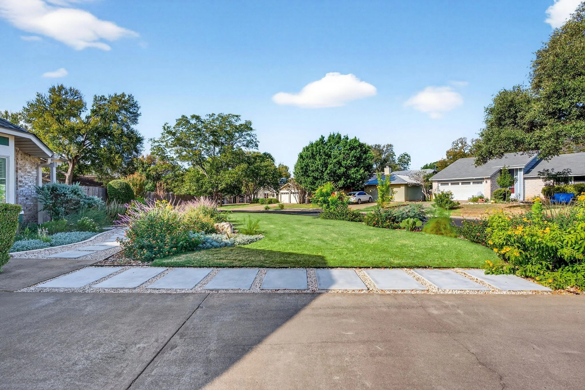 Flagstone paver path crossing a lawn to a driveway, framed by native perennial beds and mature oaks