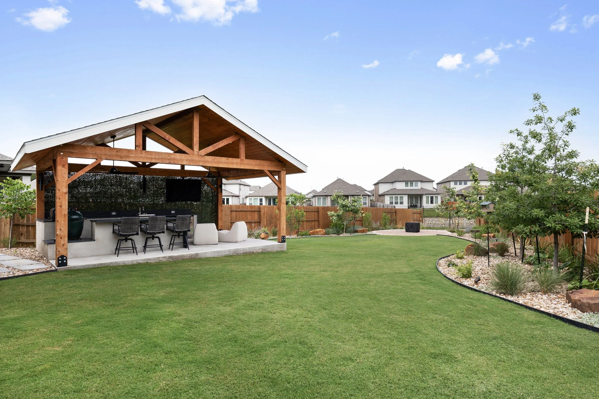 Cedar pavilion and outdoor kitchen beside a curved, steel-edged planting bed and full sod backyard