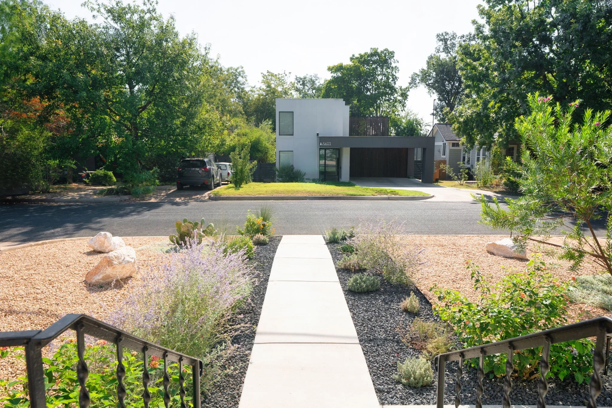 View from front porch across a xeriscaped yard with walkway, native plantings, and young shade trees