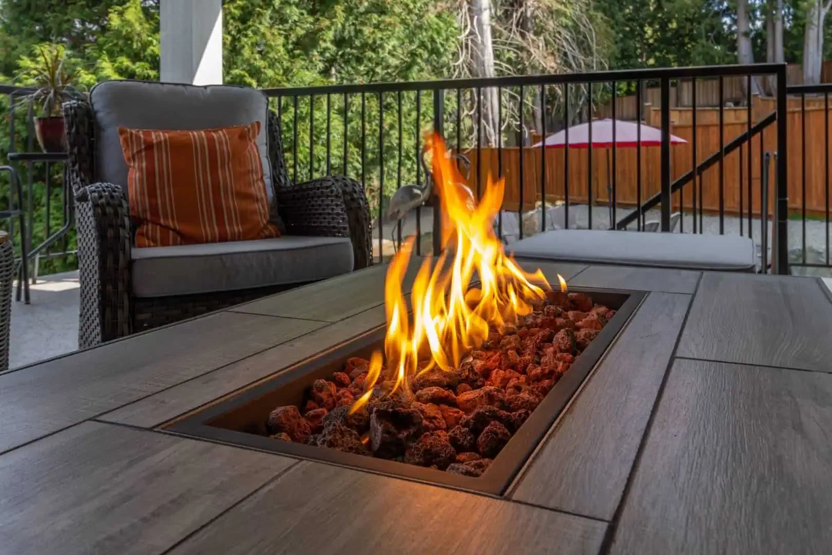 Close-up of a rectangular gas fire pit with lava rocks on a patio table, adding warmth to an outdoor seating area.