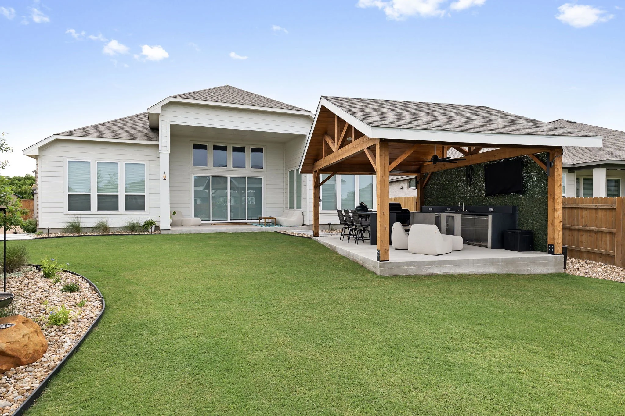Backyard makeover with covered outdoor kitchen, fresh sod lawn, and boulder-accented river rock bed