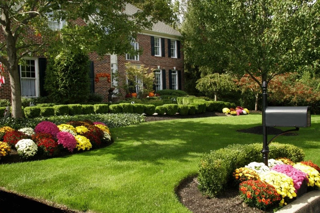 Beautifully landscaped front yard of a brick house, featuring lush green grass, vibrant flower beds, and neatly trimmed hedges.